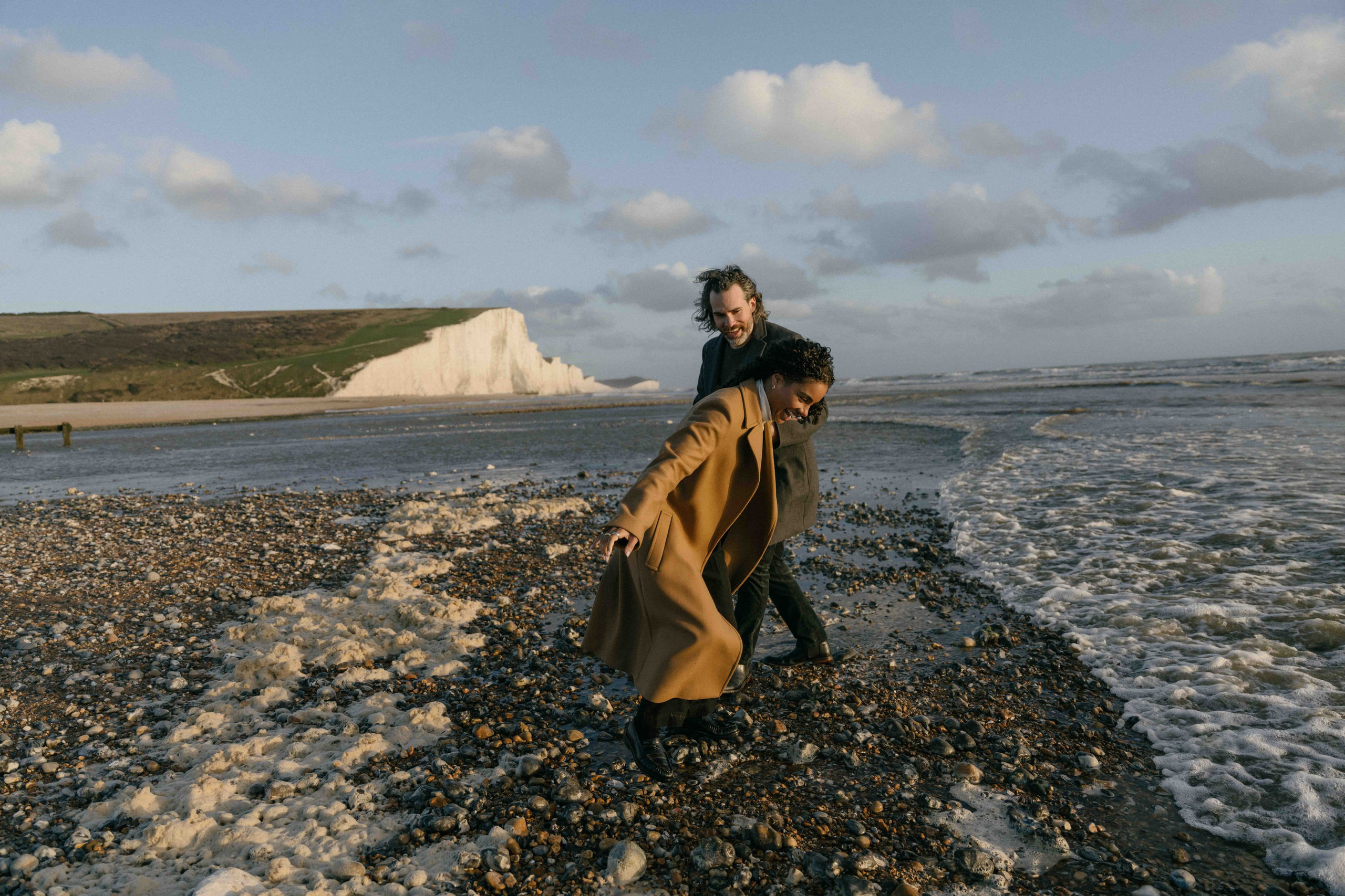 playful couple running beach seven sisters engagement photos uk