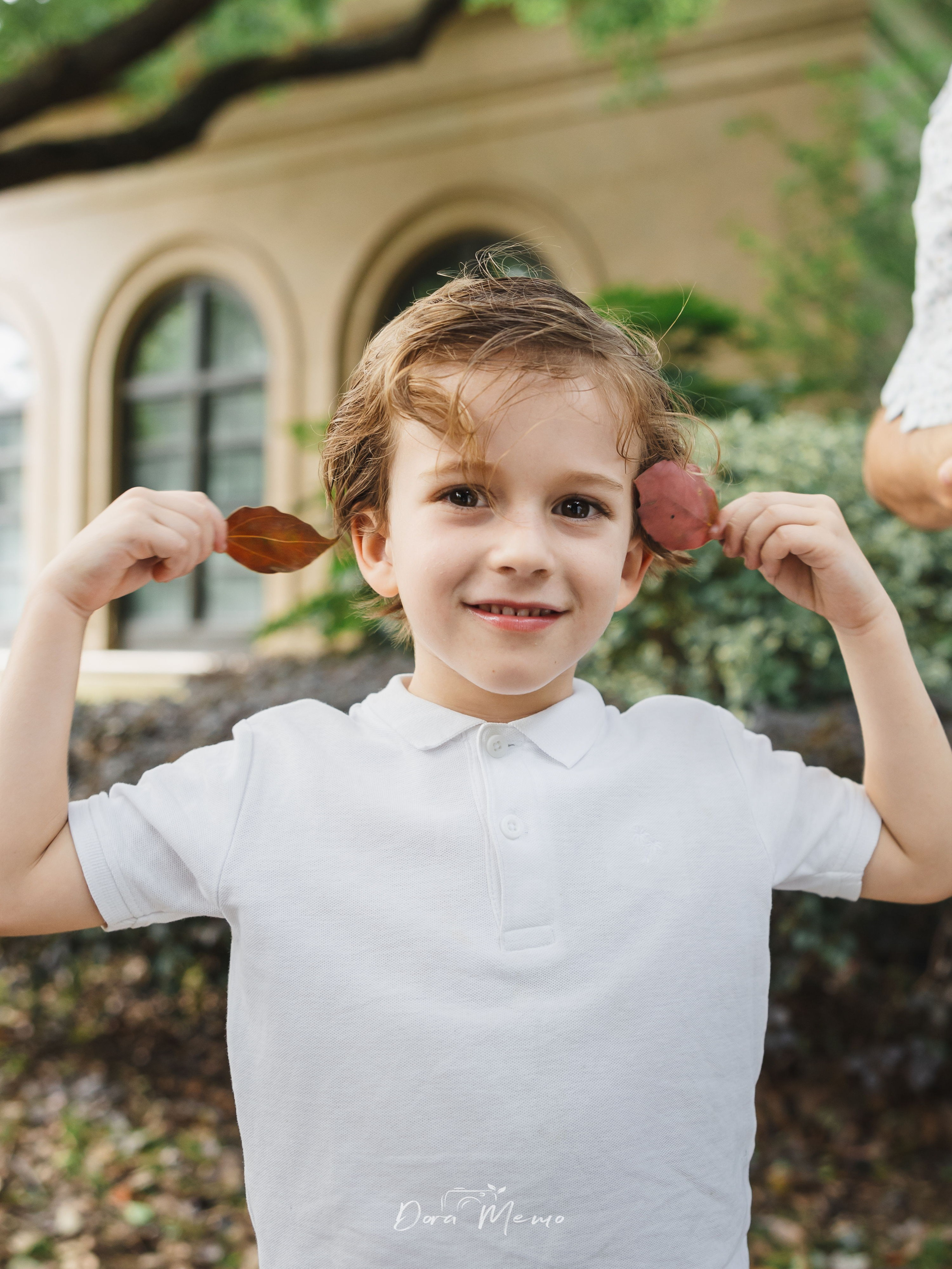 Child with leaves playfully placed on ears | A child giggling with leaves on their ears, playful and carefree