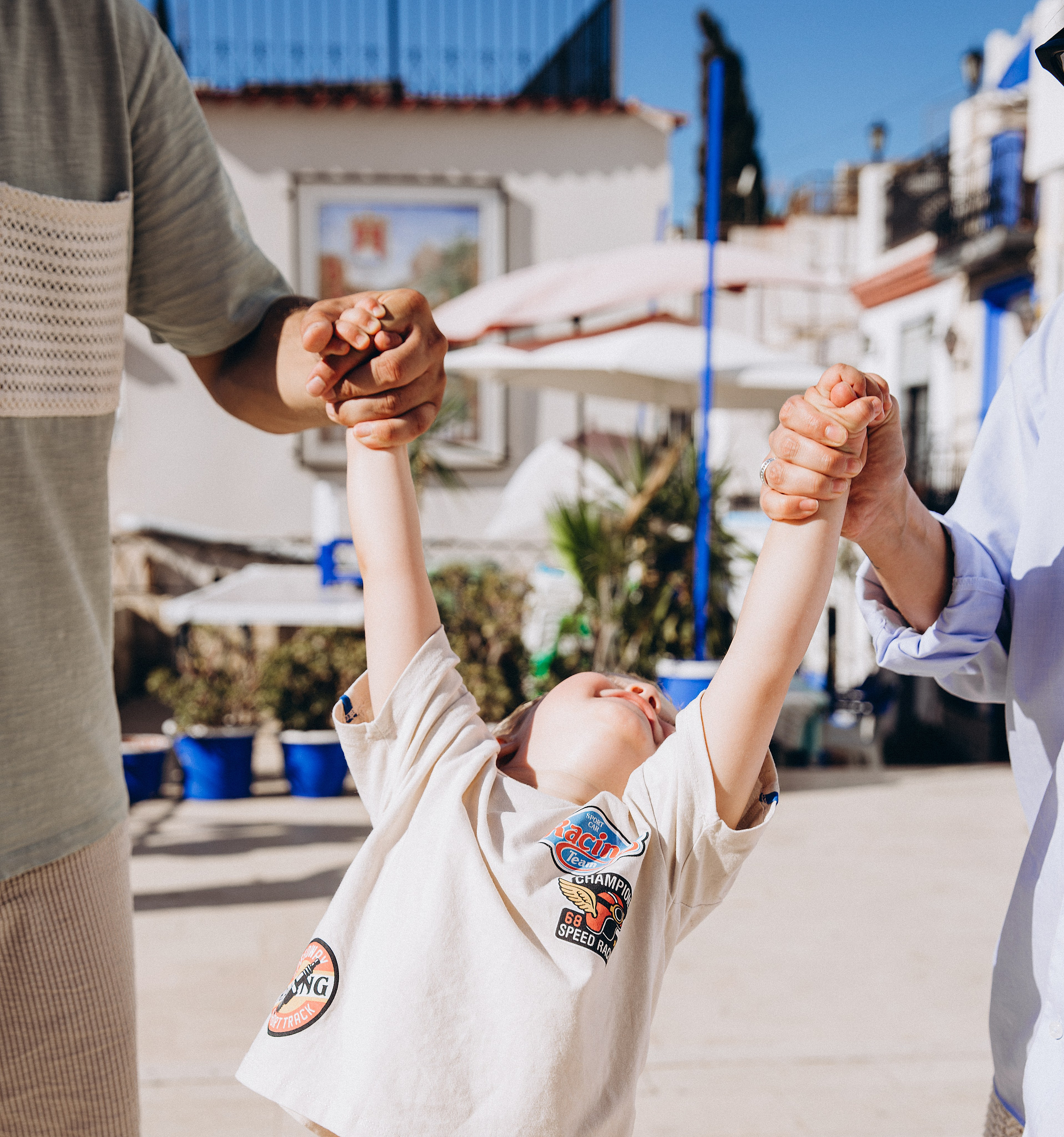 Alegre sesión familiar en Valencia, España — momento espontáneo de un niño riendo mientras es levantado por ambos padres, capturando felicidad pura y conexión. Ideal para familias que buscan fotografía familiar lúdica y natural en Valencia y España.