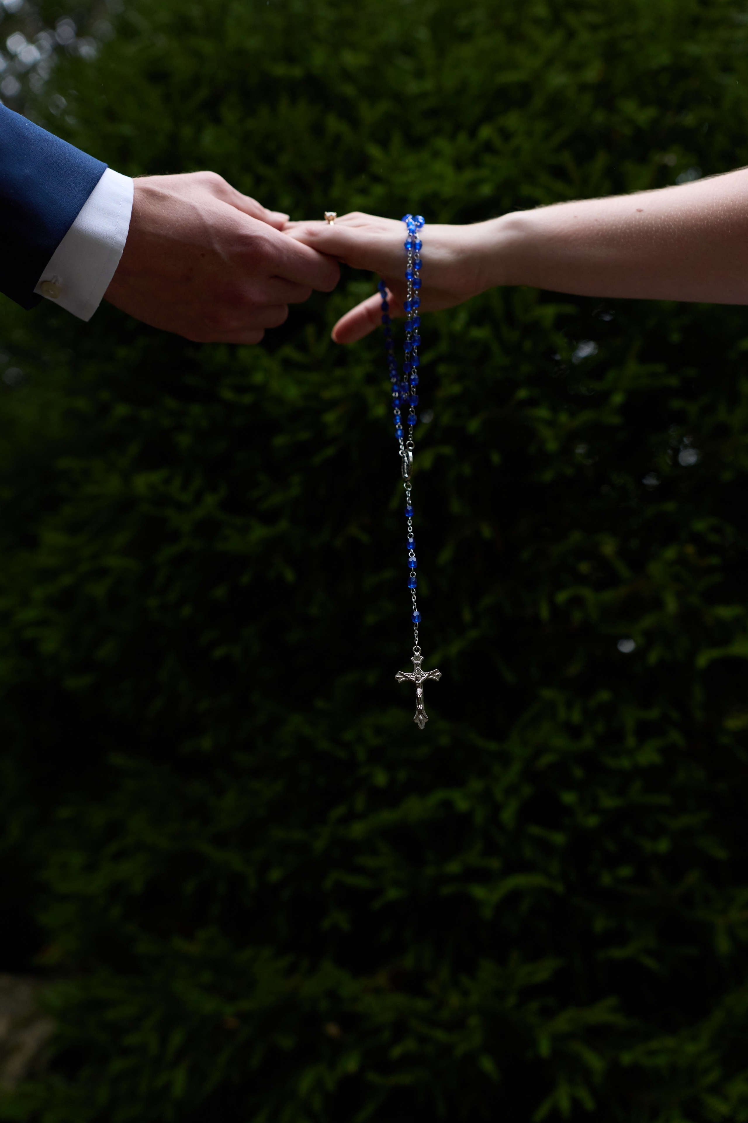 Rosary held between their hands against dark foliage at Inniswood Metro Gardens