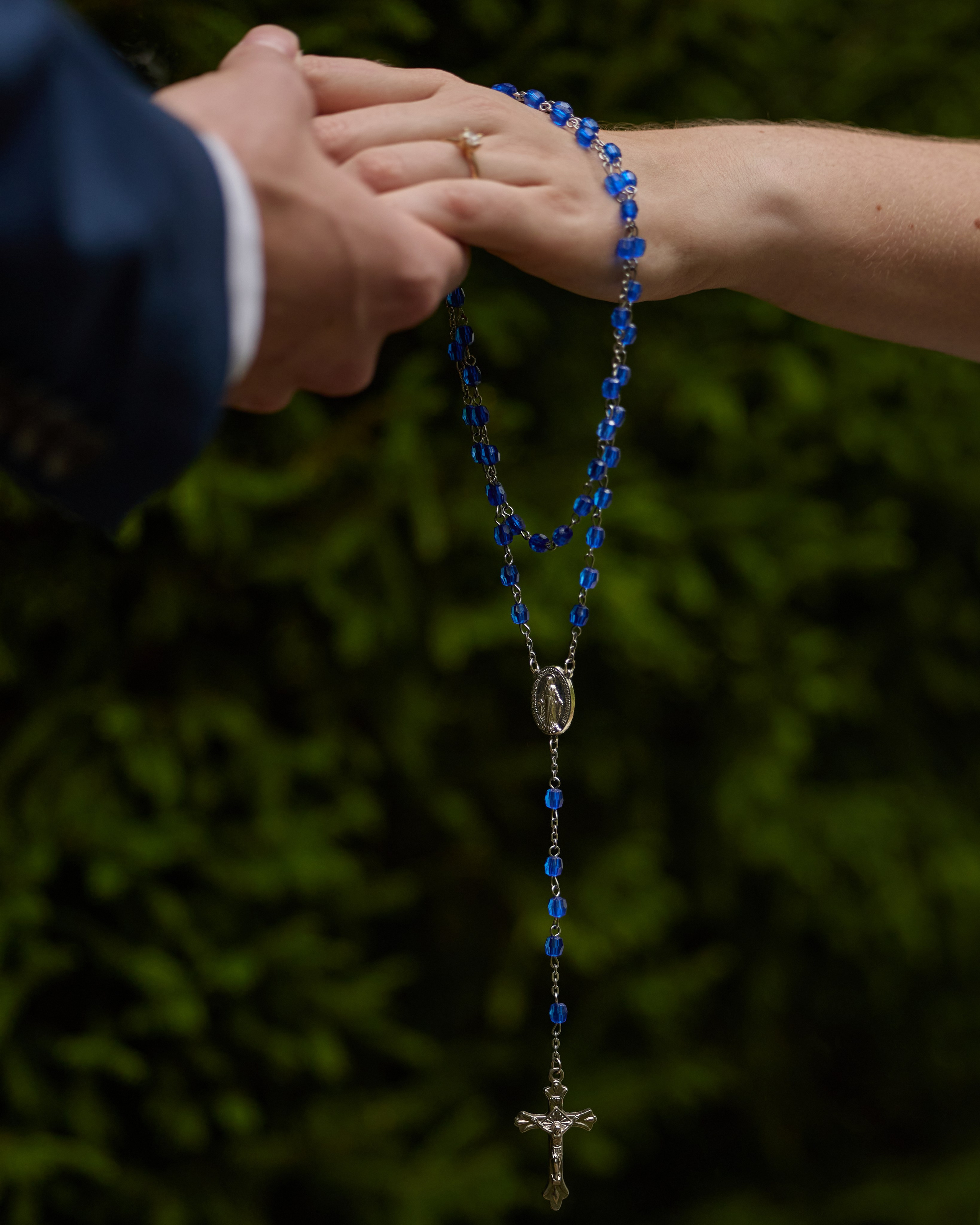  Close-up of hands holding a blue rosary during an engagement shoot in Ohio