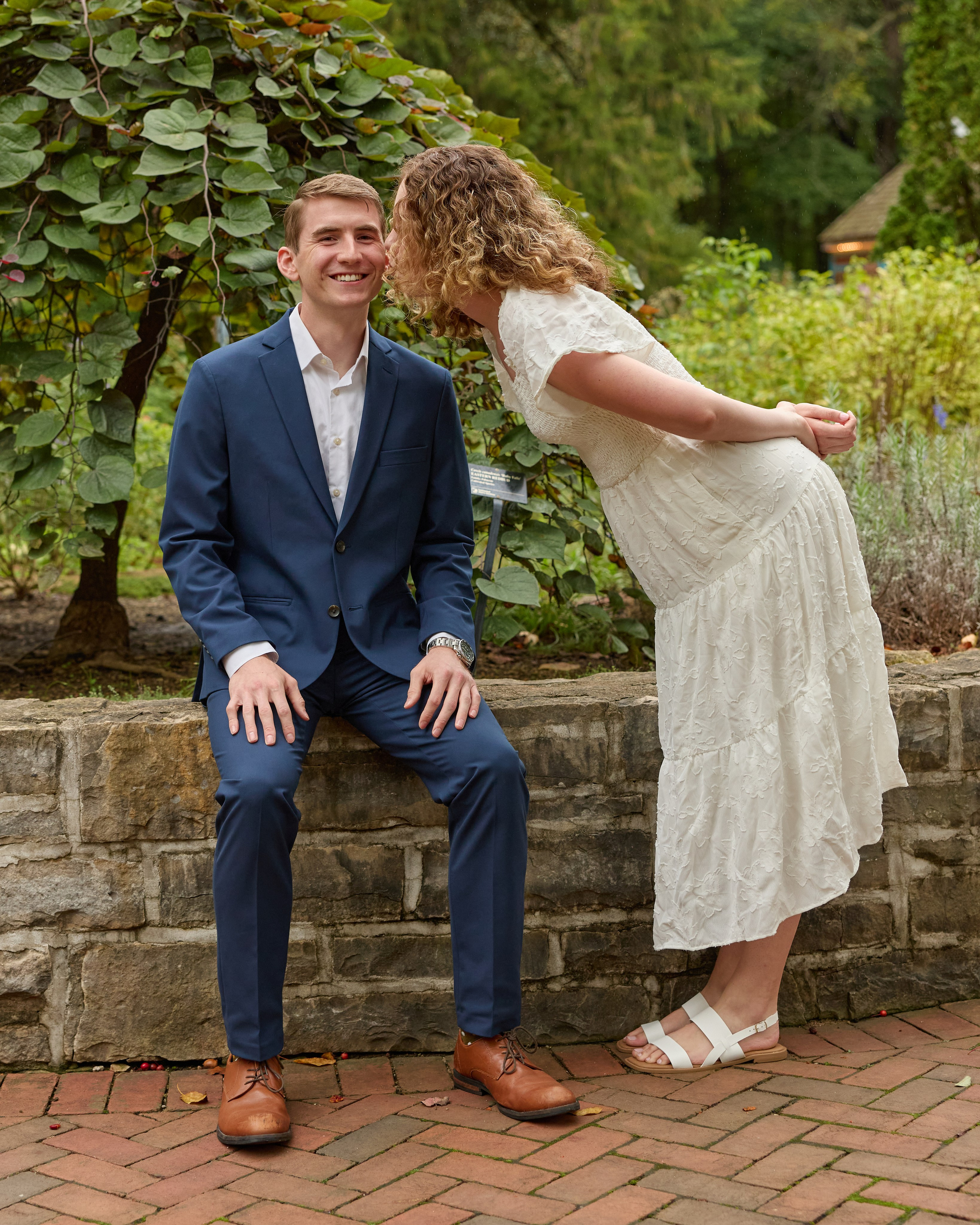 She leans in to kiss him as he sits on a stone wall at Inniswood, Ohio