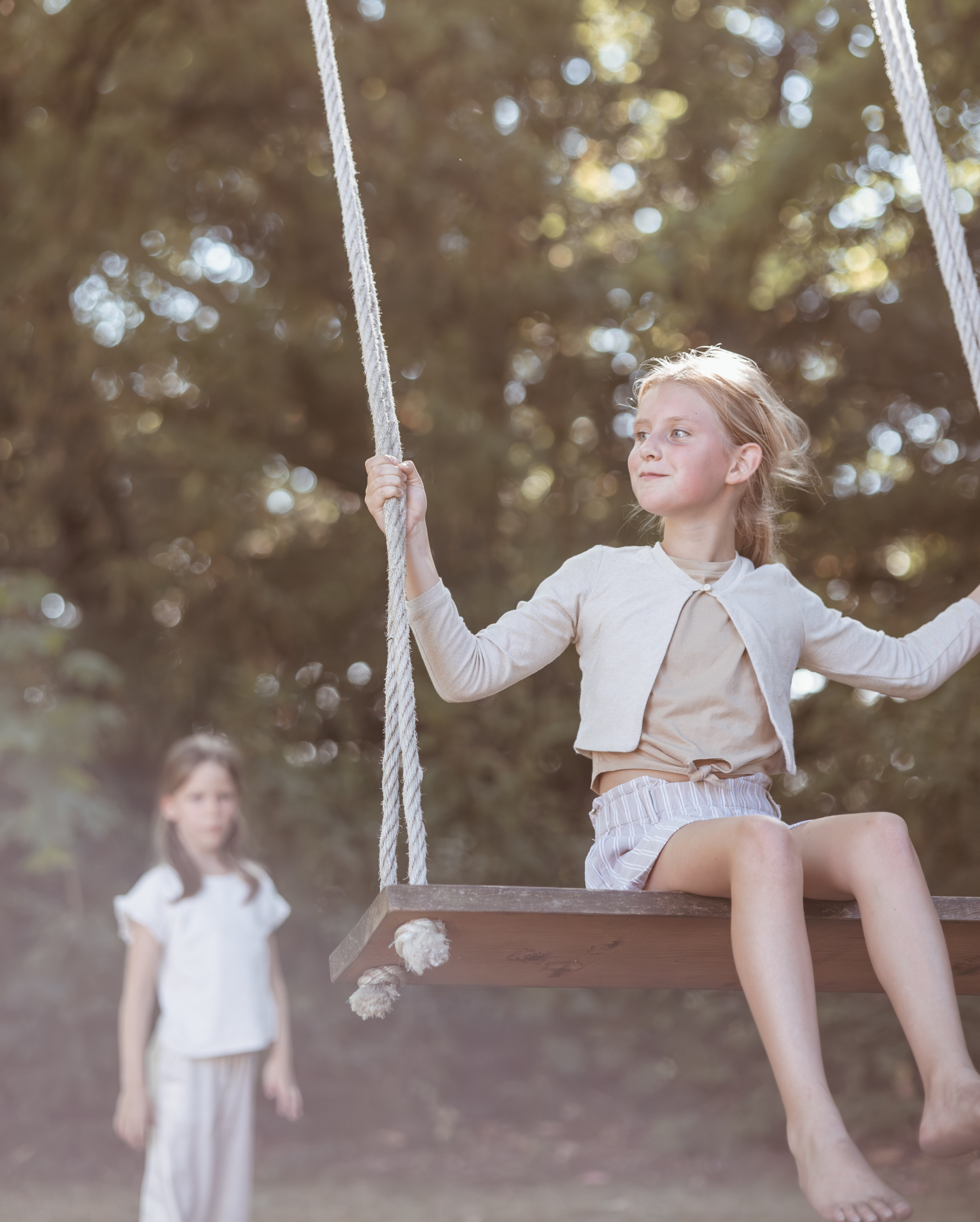 Twee meisjes lachen samen op een schommel tijdens een speelse buitenfotoshoot door Kapture Fotografie