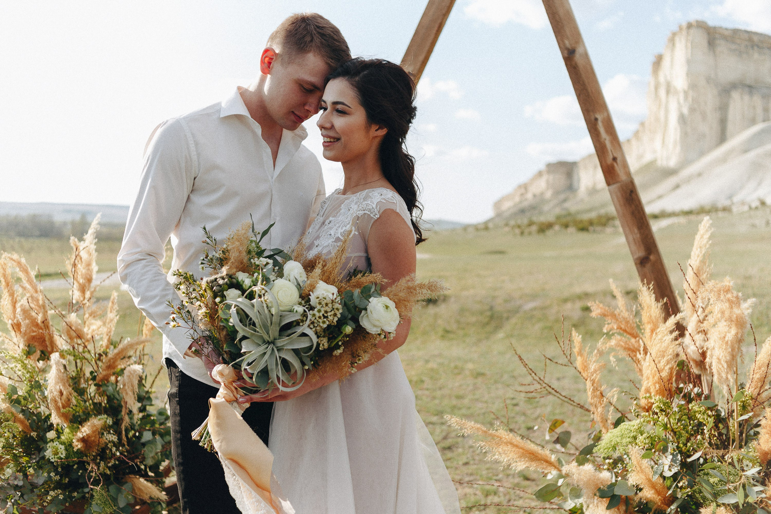 Bride and groom smiling with bouquet outdoors, joyful wedding portrait