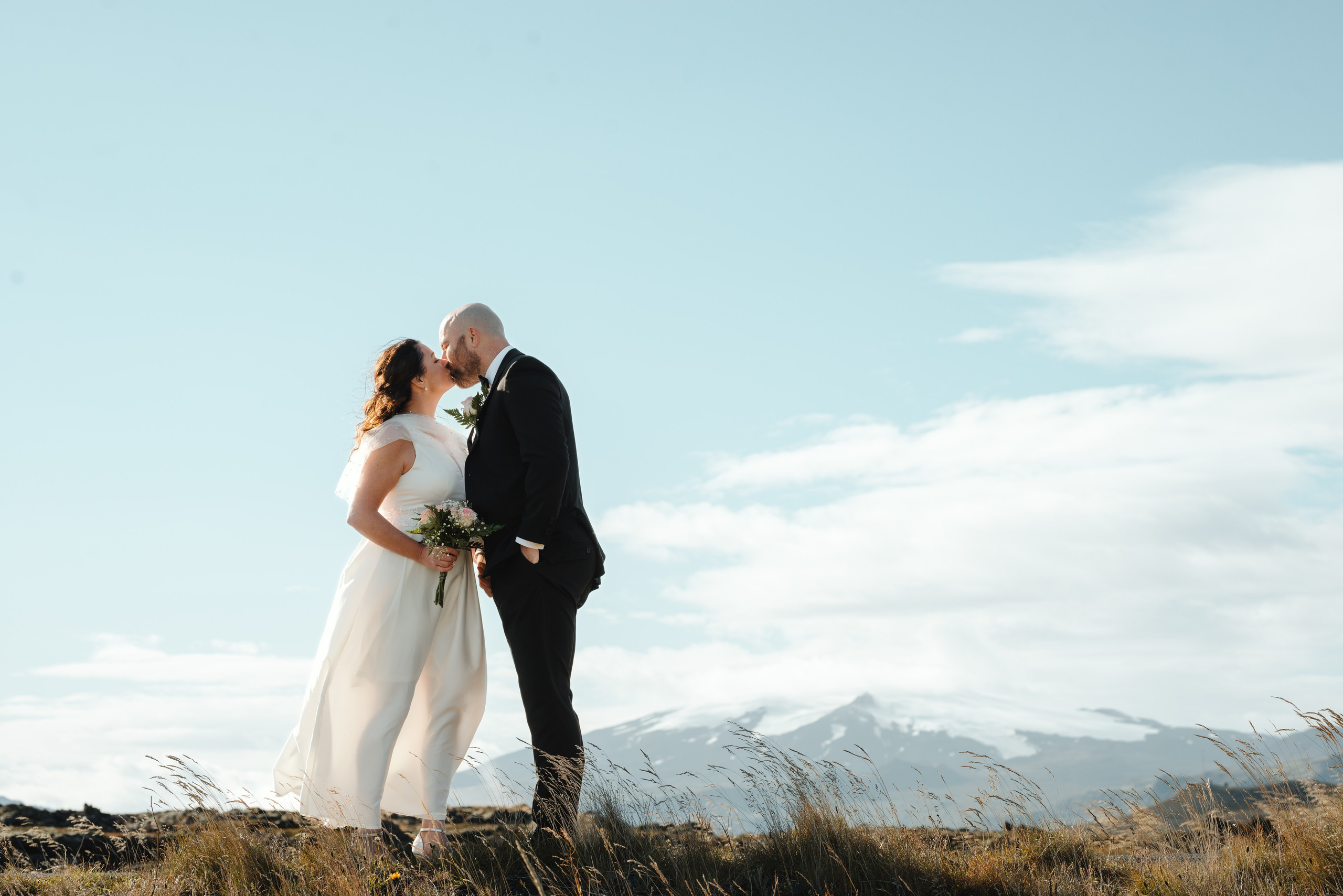 Bride in a flowing dress, gently petting a sheep near the rugged coastline of Snæfellsnes.