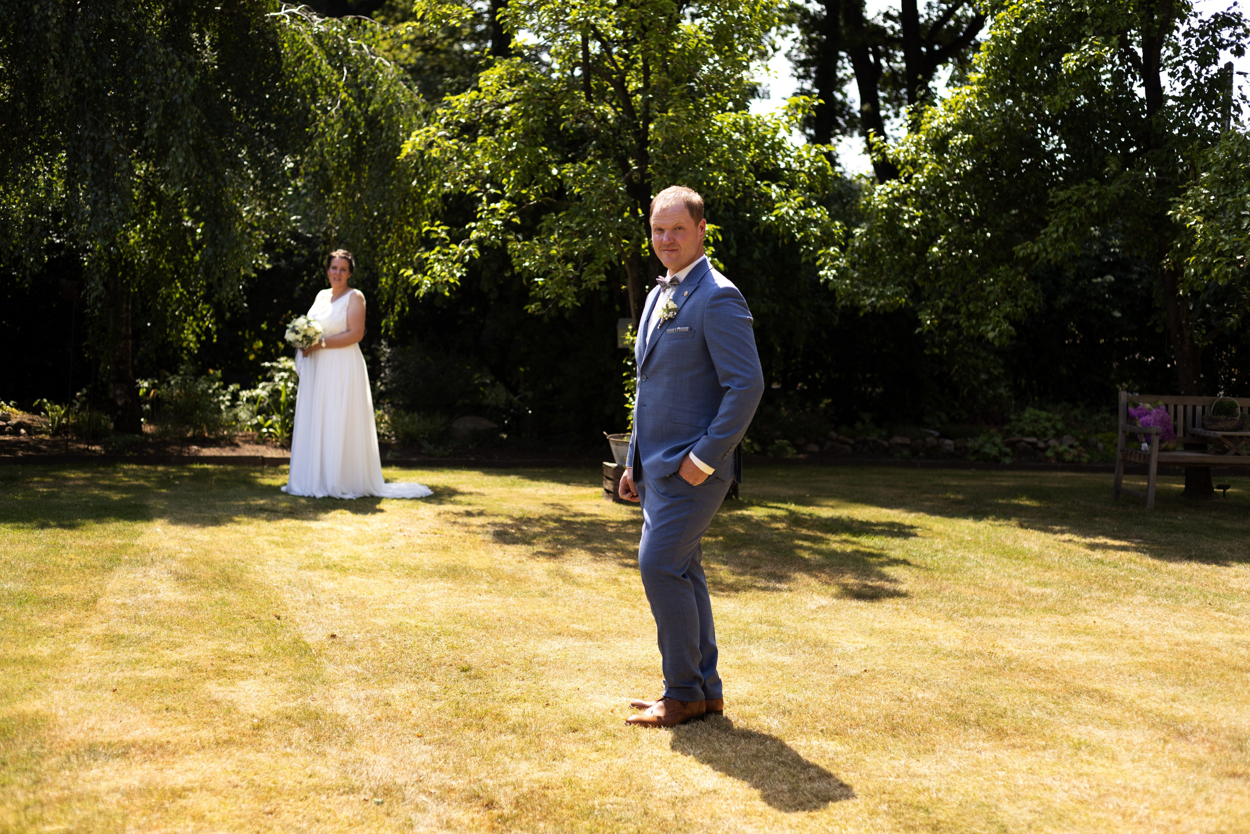 Brautpaar bei einem rustikalen Fotoshooting auf einem Feld mit Strohballen, umgeben von Natur.