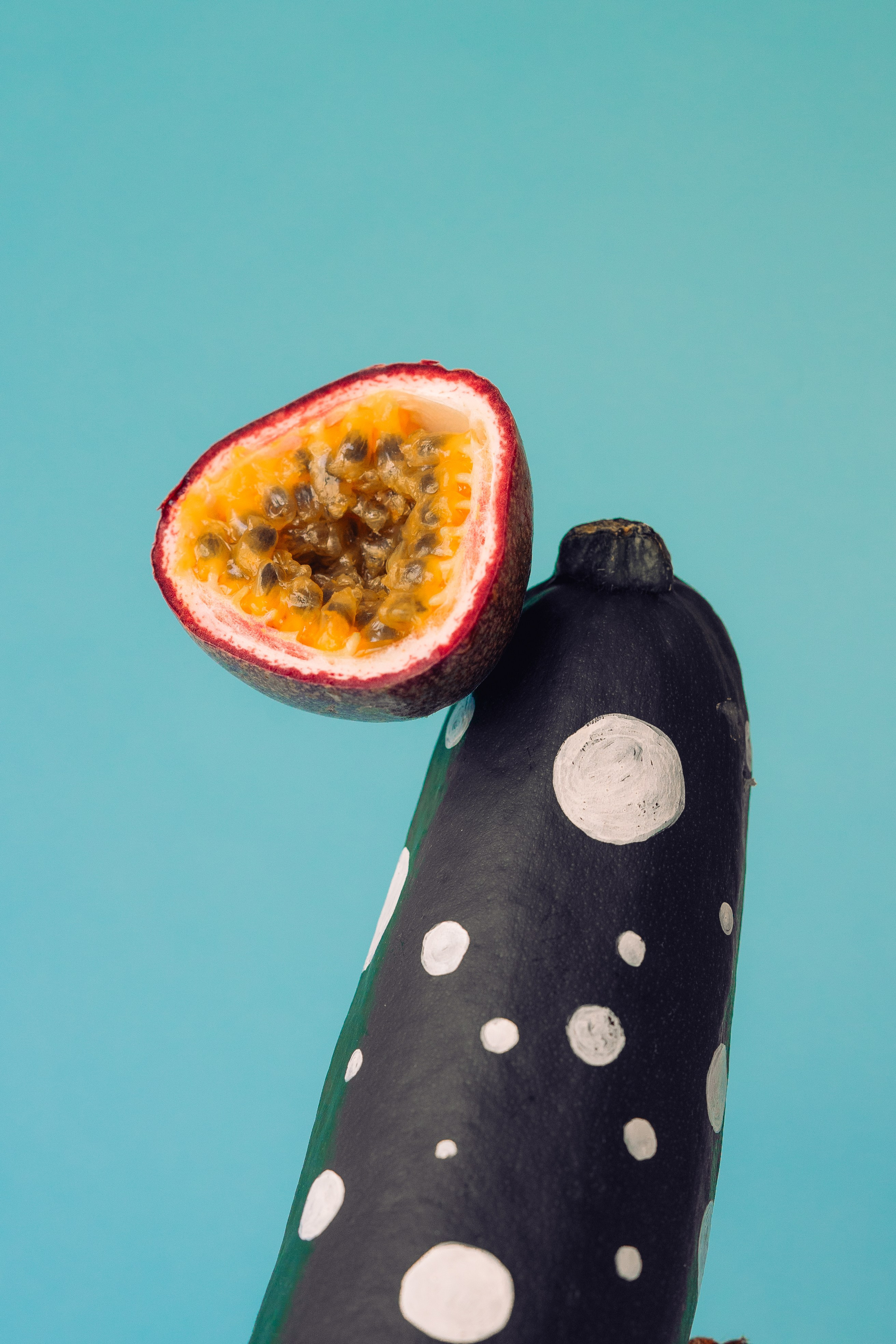 Dotted Design Painted Passion Fruit and Courgette. Creative display of dotted design painted maracuja and zucchini on a bright blue backdrop.