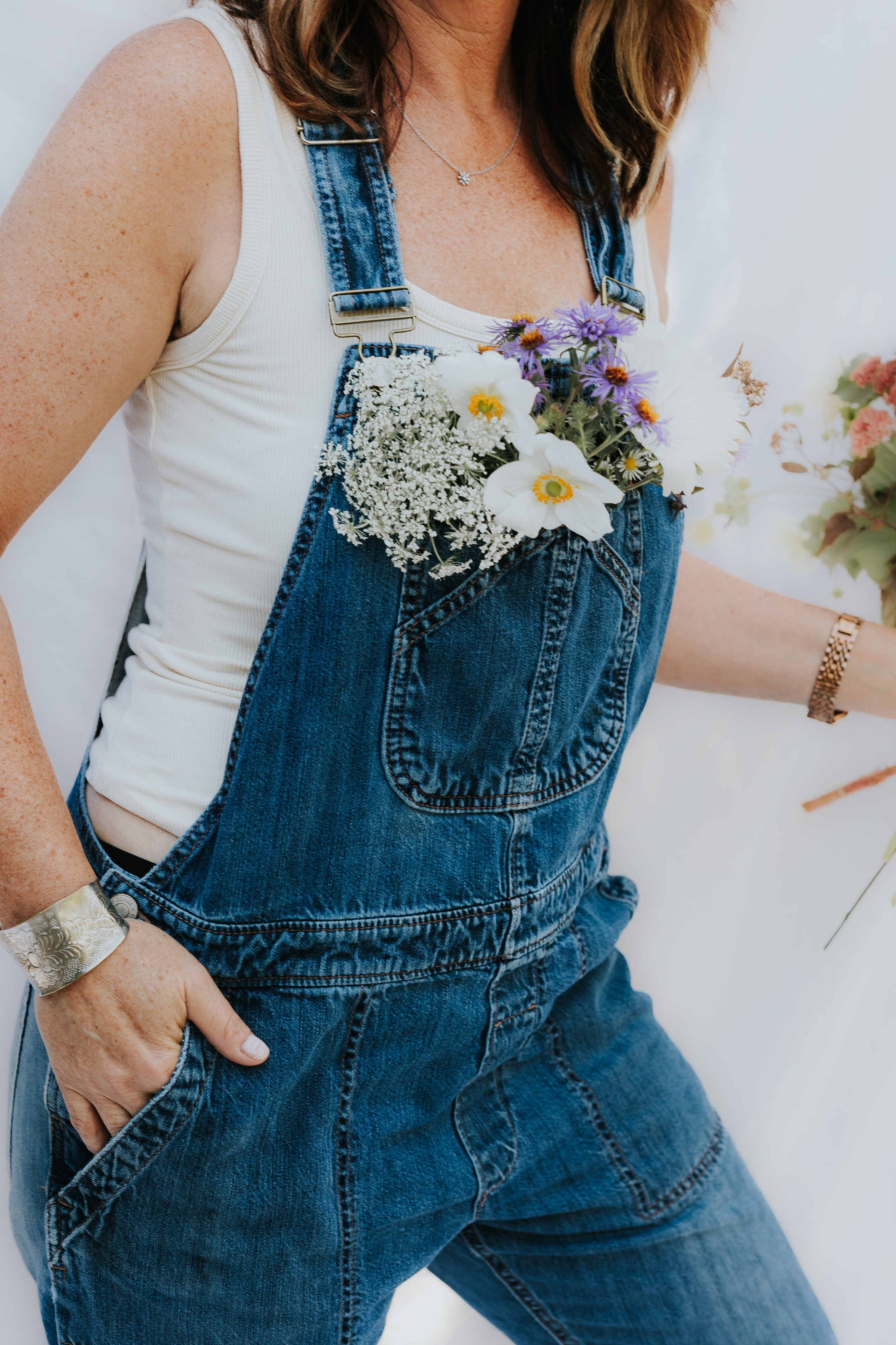 Woman in overalls with flowers stuffed in pocket of overalls 