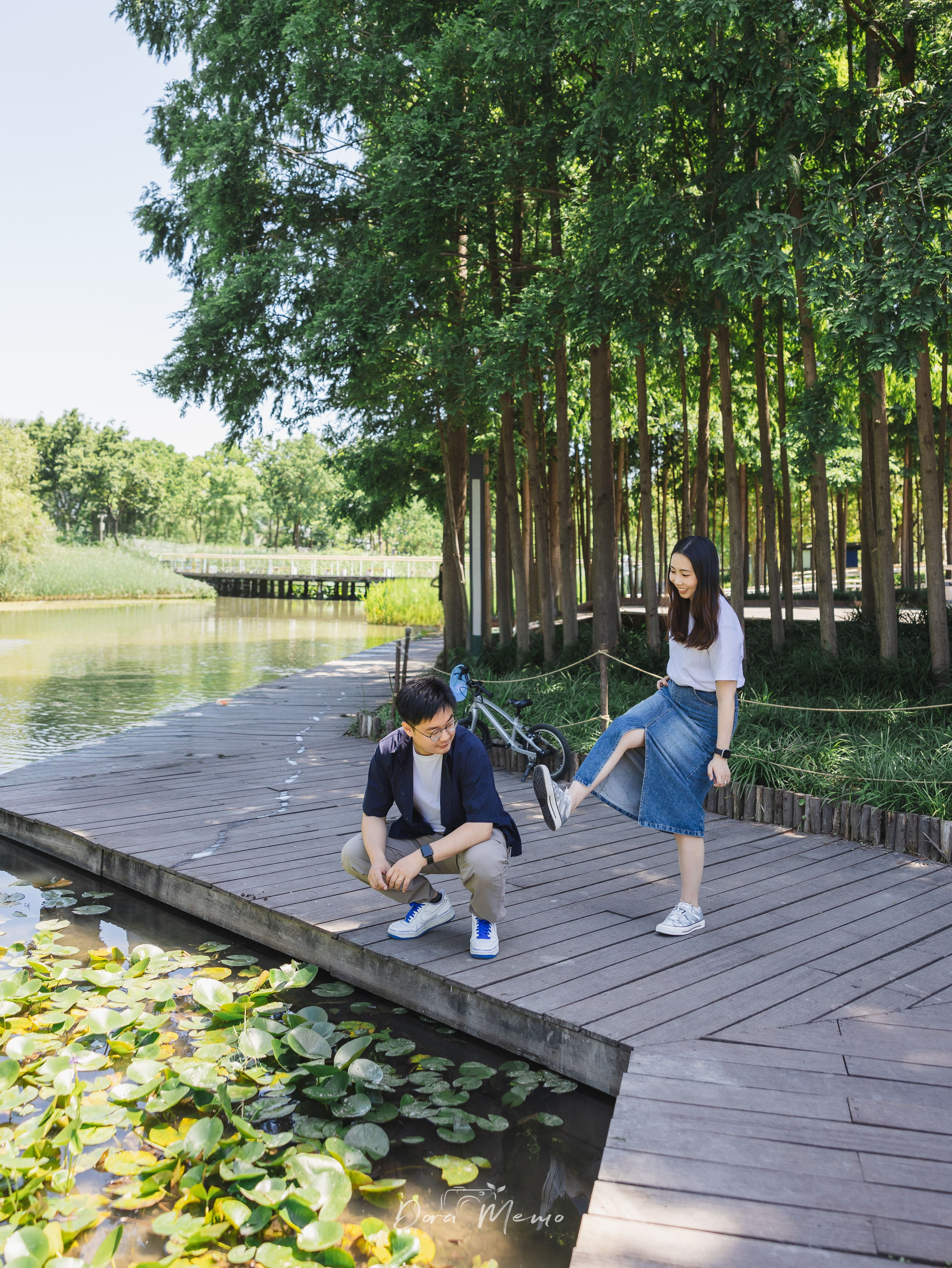 Couple being playful on a wooden dock by a pond, lily pads and bicycle nearby 