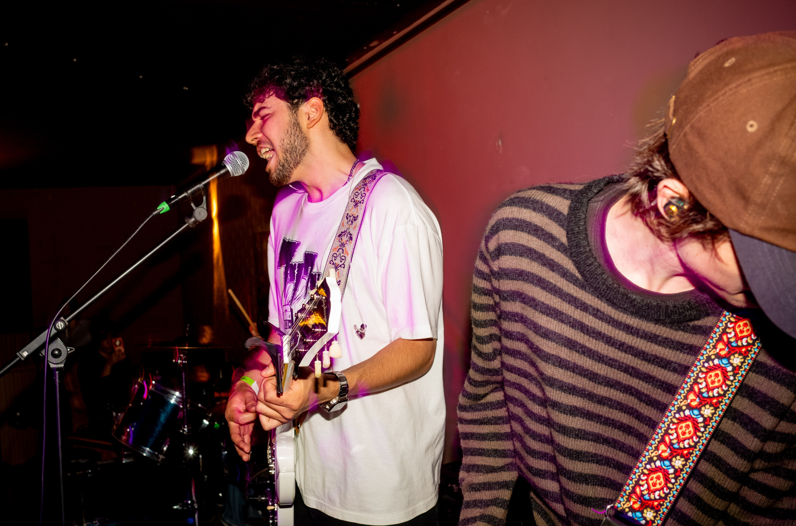 Keyingi Safar: guitarist singing at the microphone beside a bassist in a striped sweater — Boshqa Musiqa Fest, Ponaexali Hall, Tashkent, September 2026