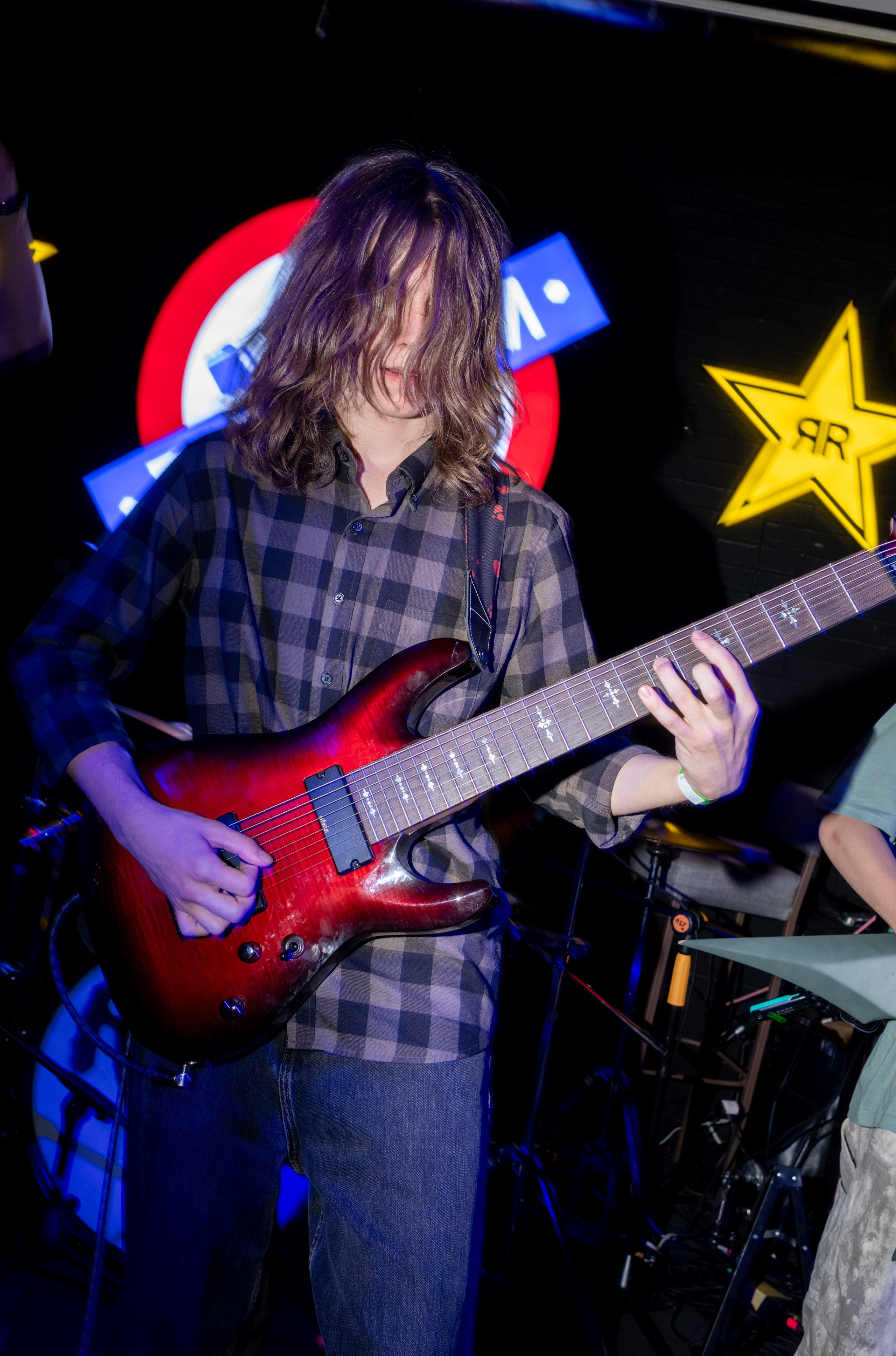 Ebdromeer: long-haired guitarist in a plaid shirt playing a red guitar — Boshqa Musiqa Fest, Ponaexali Hall, Tashkent, September 2026
