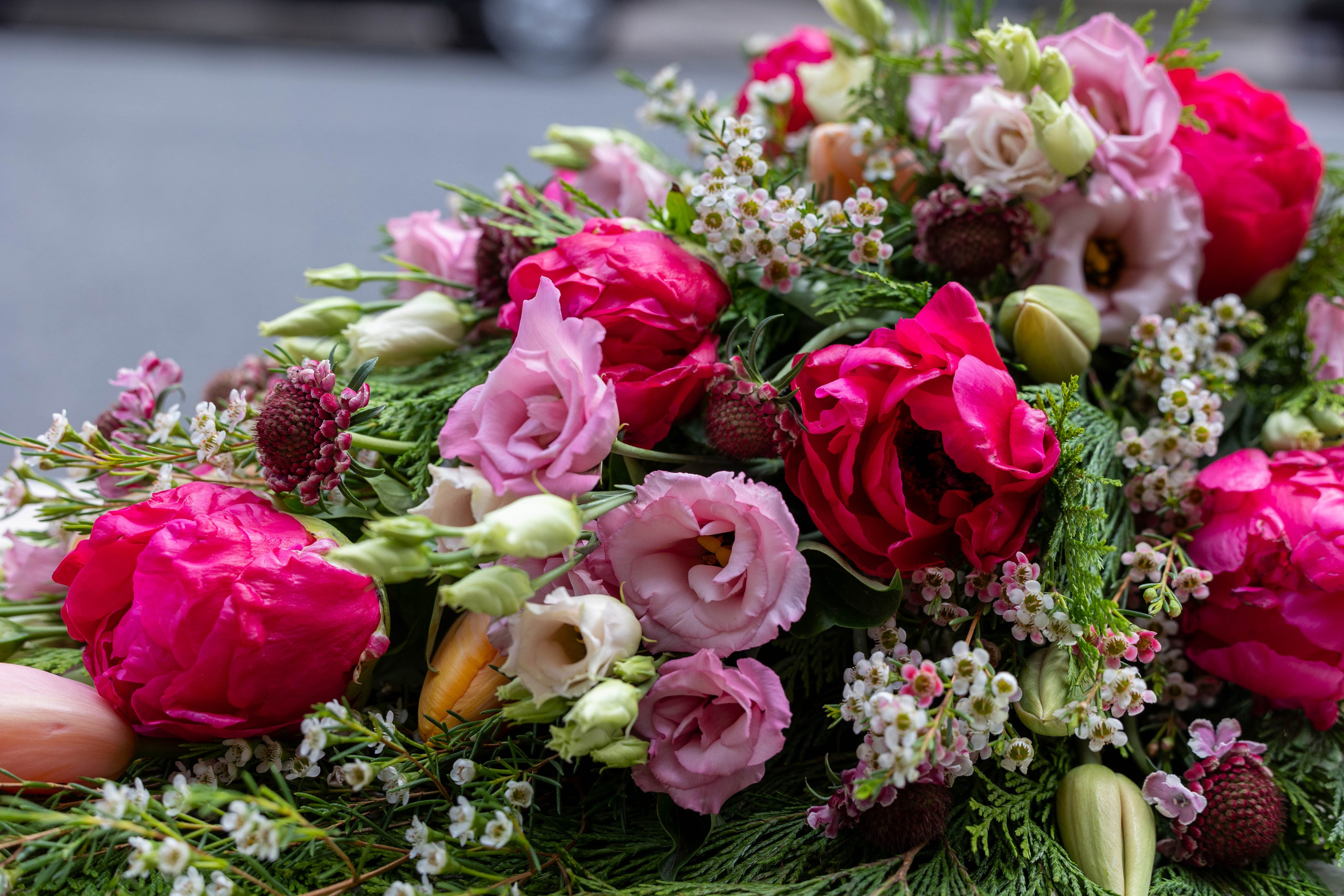 En let og luftig bårebuket, hvor blomsterne er bundet i liggende position. Hver blomst fremhæves smukt med varierede grønt imellem. Bårebuketten er bundet med pink, hvilket lyser ethvert kirkegulv i enhver sæson.