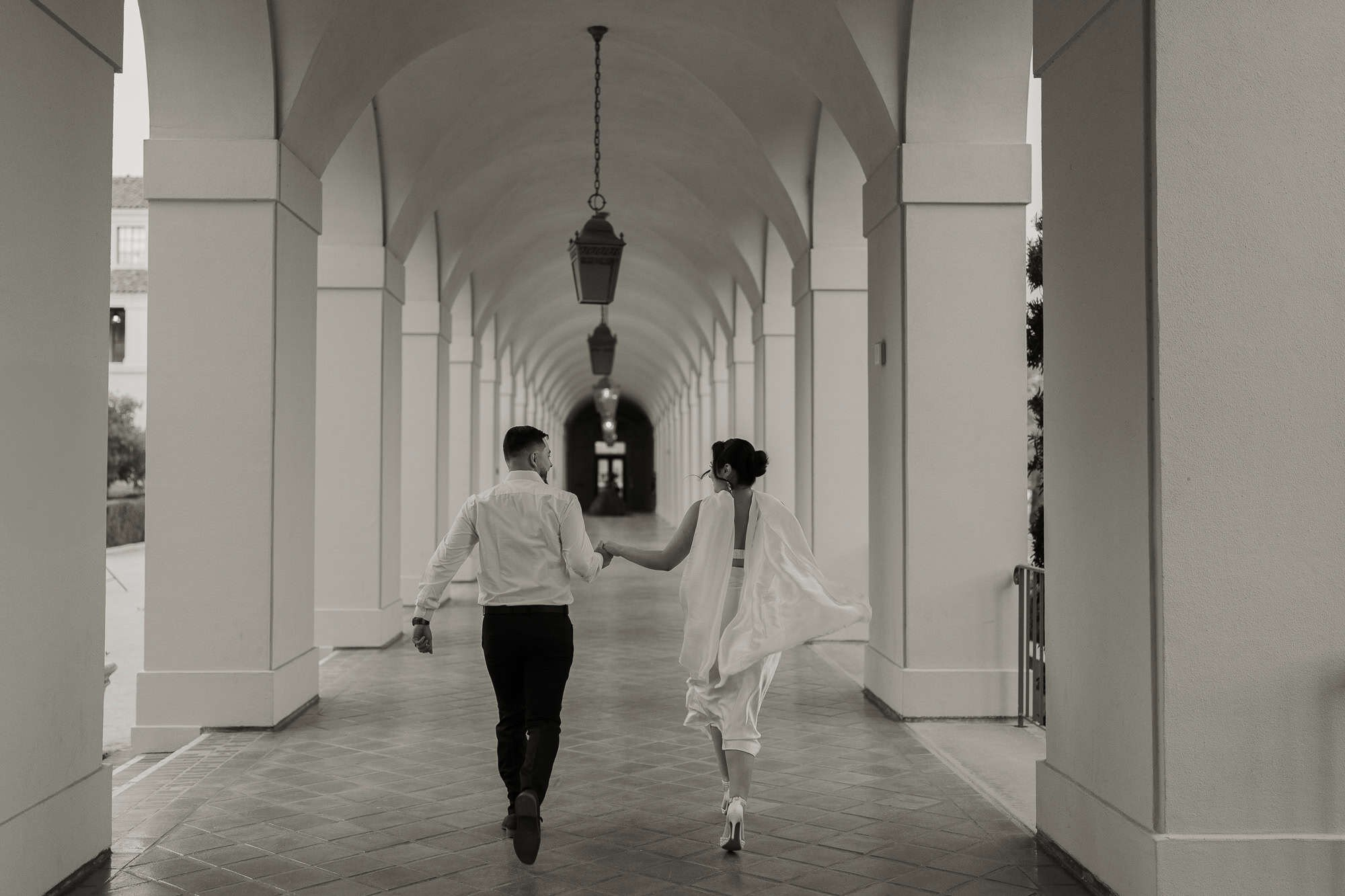 Black and white photo of newlyweds walking through arched corridor in Pasadena City Hall