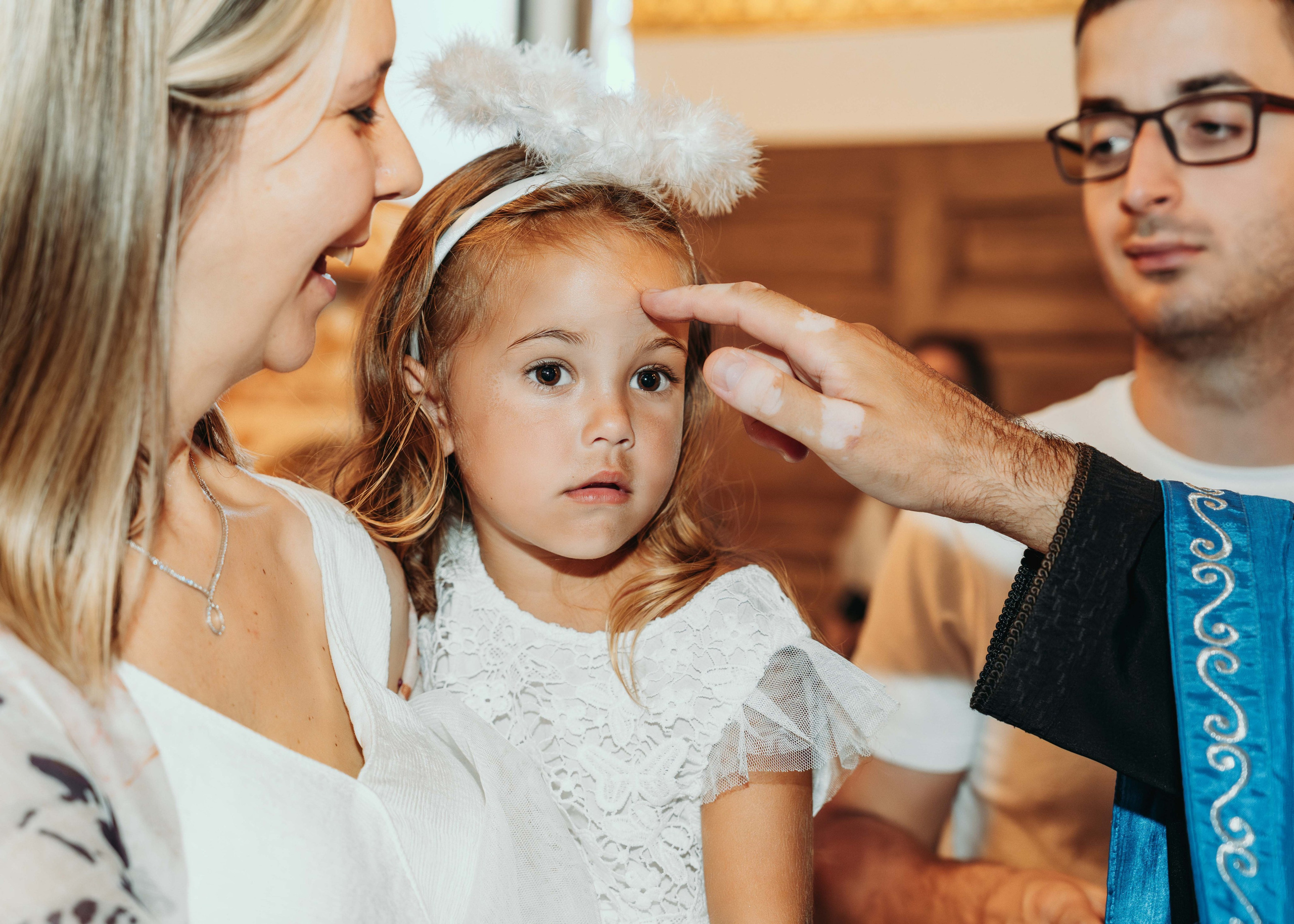 Svestenik pomazuje devojcicu sa zlatnom kosom i belom haljinom