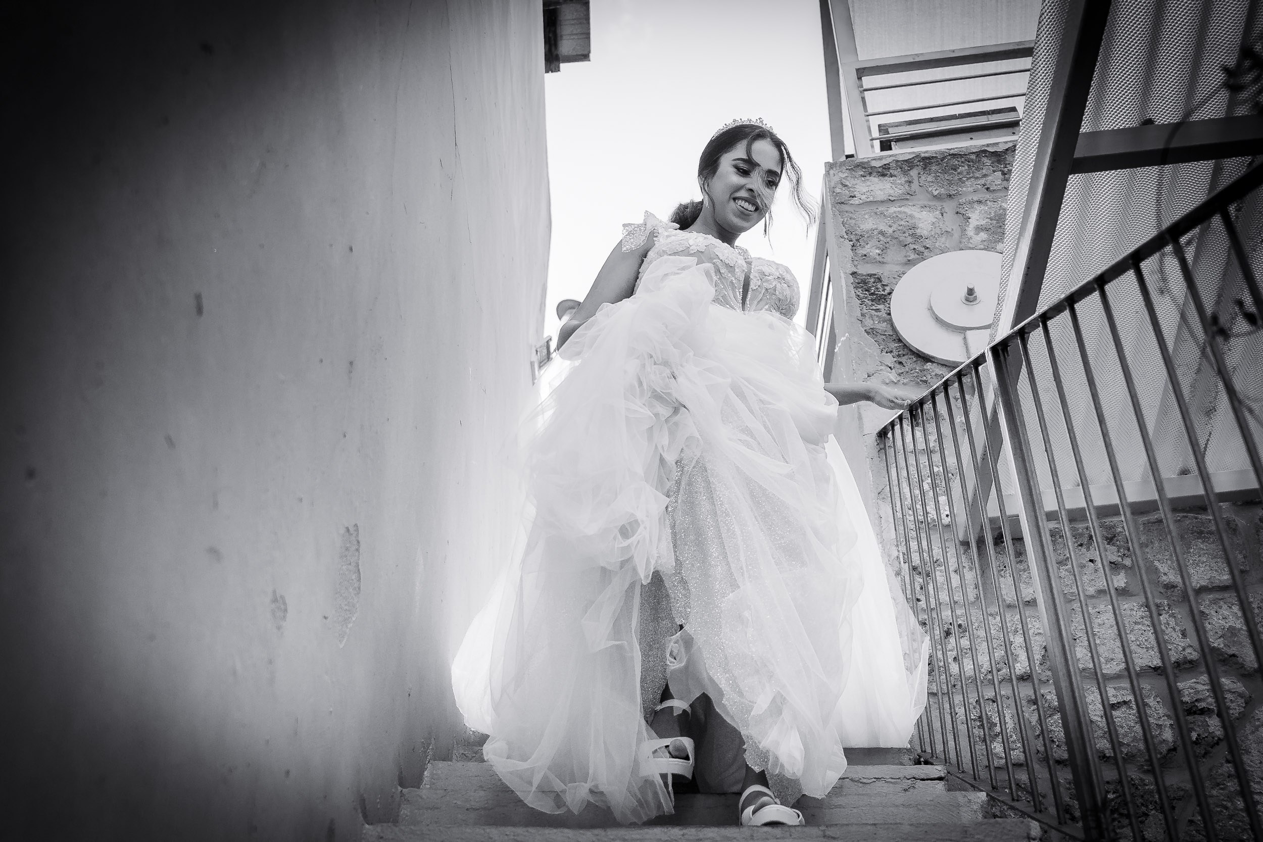 Smiling bride in a beautiful white wedding gown walking down a stone staircase in Israel