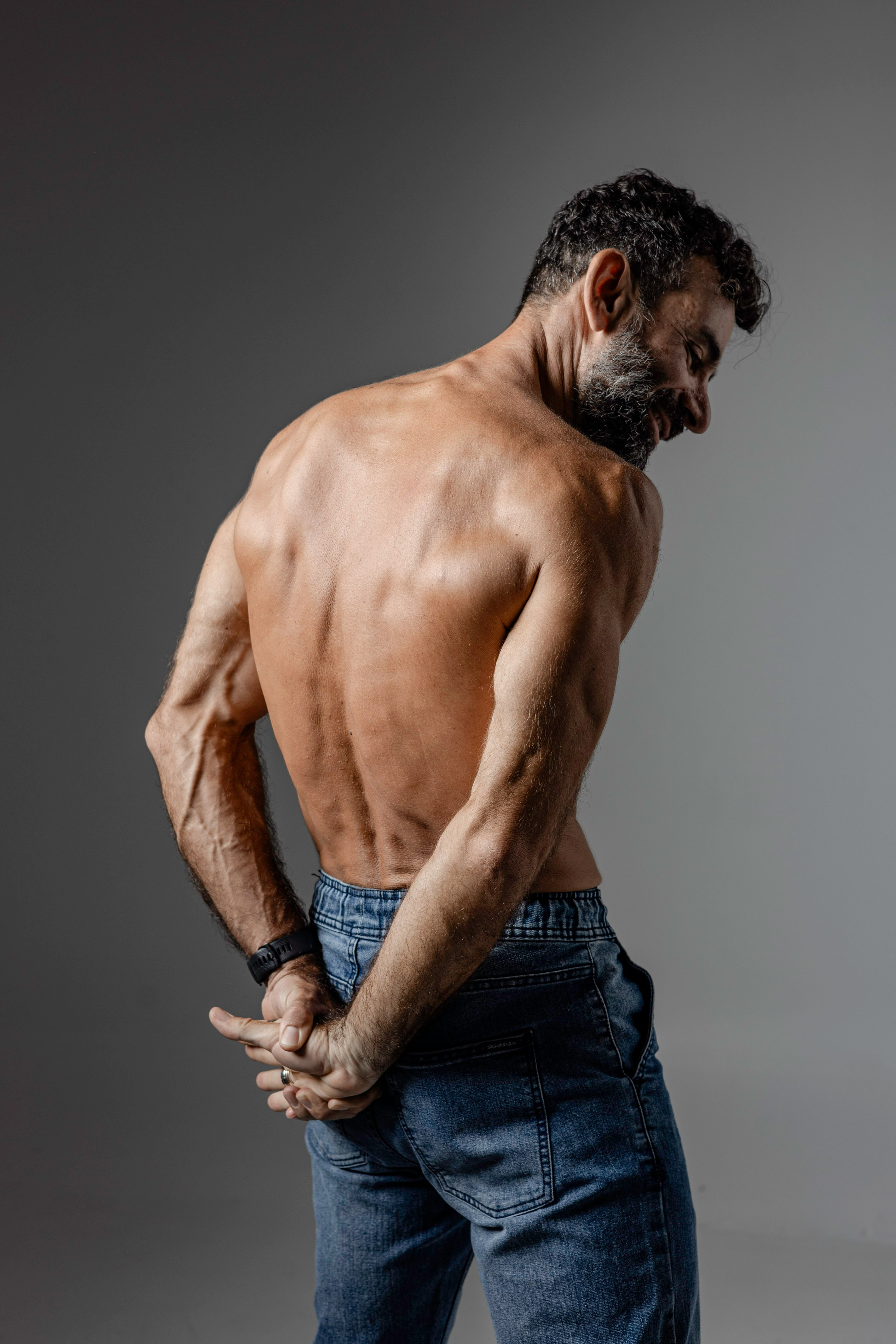 Rear-view fitness portrait of a shirtless man standing in jeans
