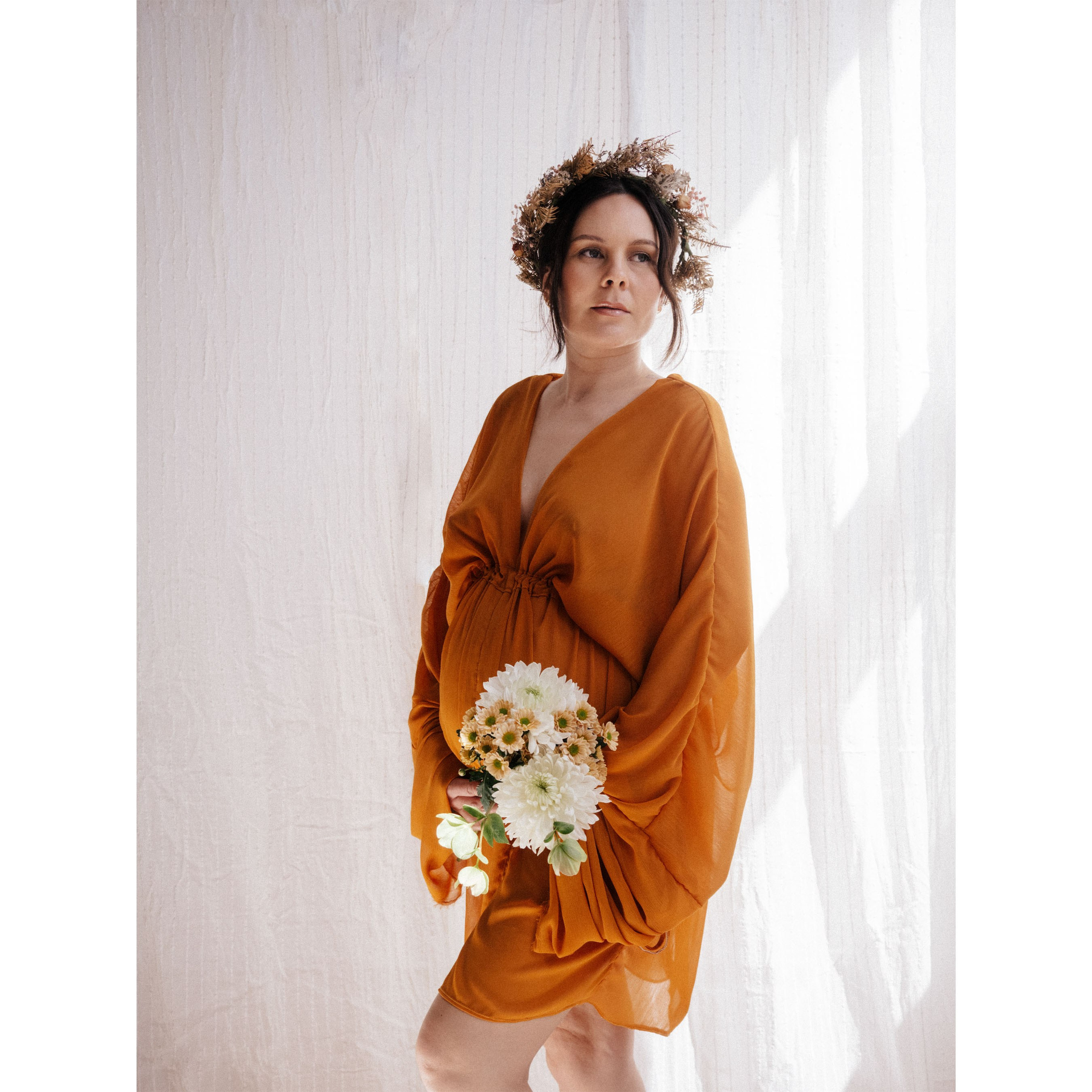Pregnant woman in elegant dress holding flowers.