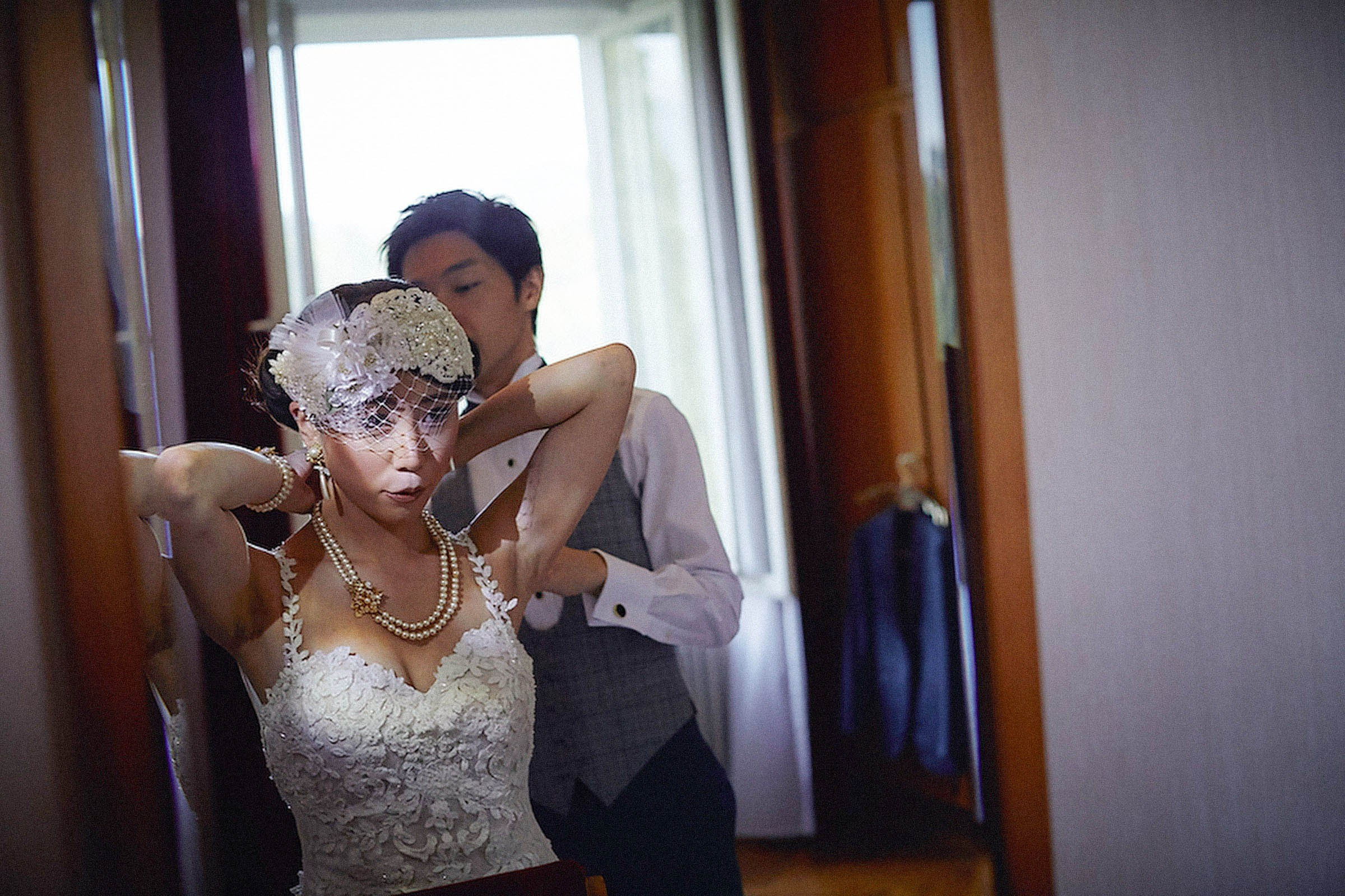 Groom assisting bride with pearl necklace during bridal prep.