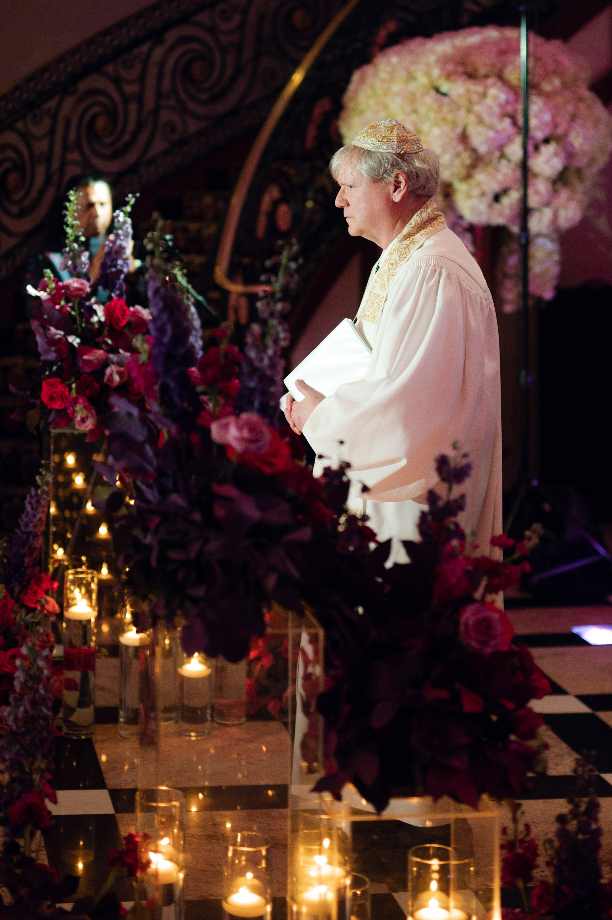 a priest is standing in front of a bunch of flowers