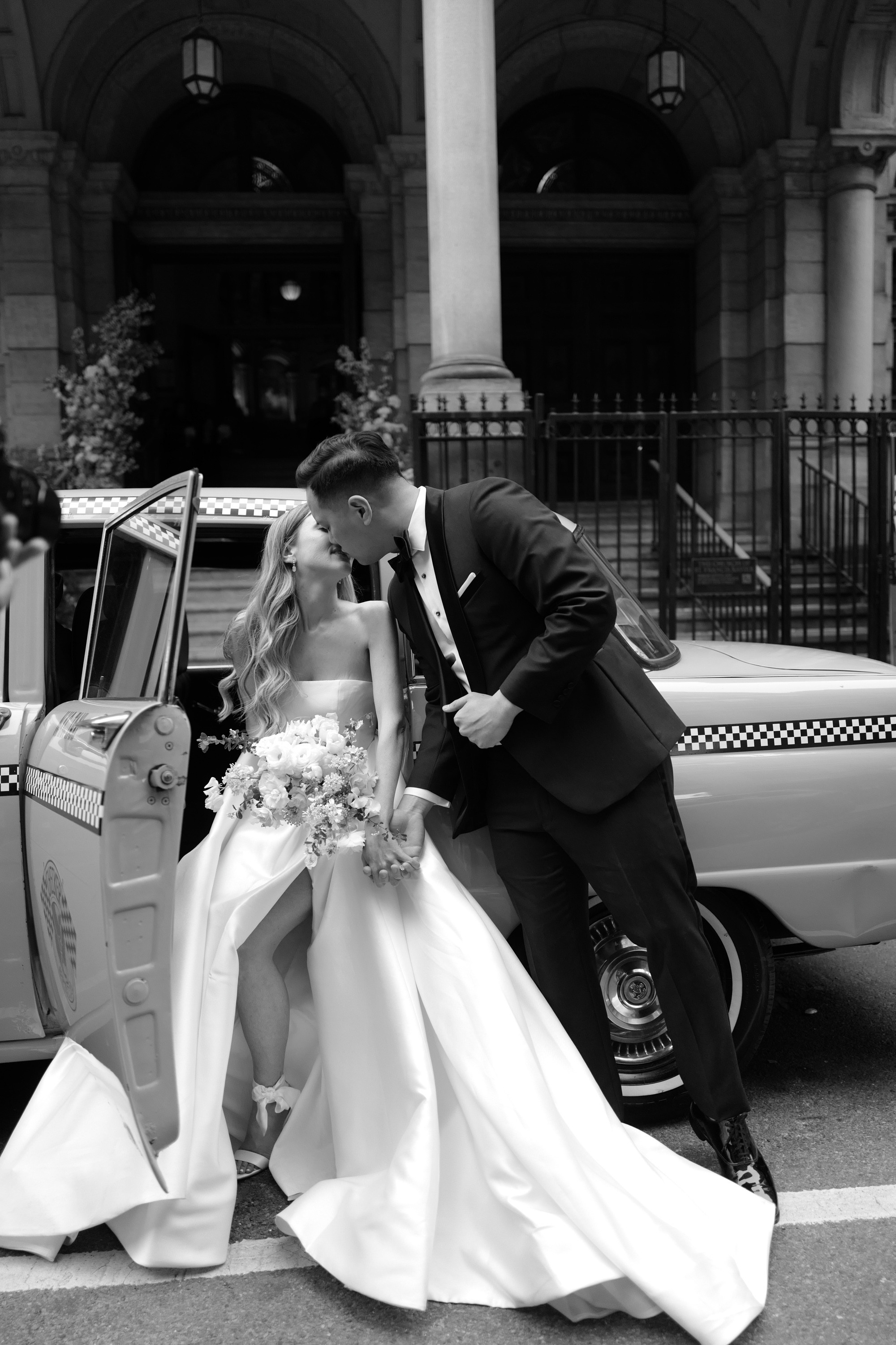 a bride and groom kissing in front of a taxi