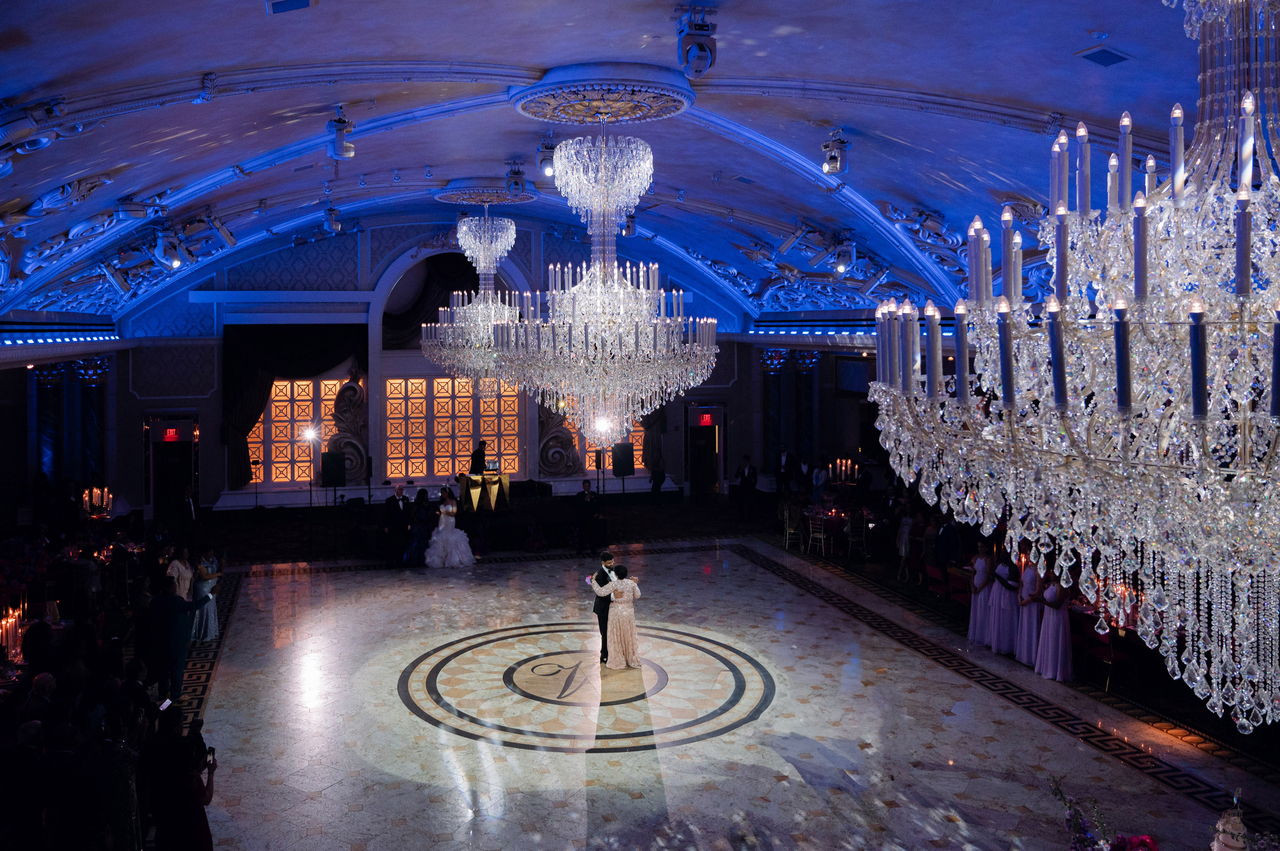 a couple standing in a large ballroom with chandels