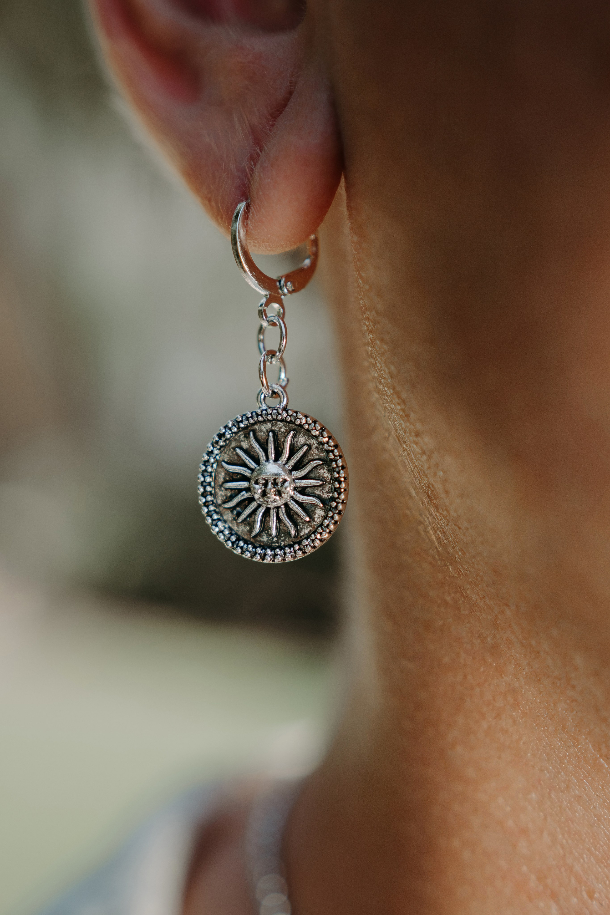 Close-up of a silver sun-shaped pendant earring, highlighting intricate craftsmanship and artistic jewelry design.Close-up of a silver sun-shaped pendant earring, highlighting intricate craftsmanship and artistic jewelry design.