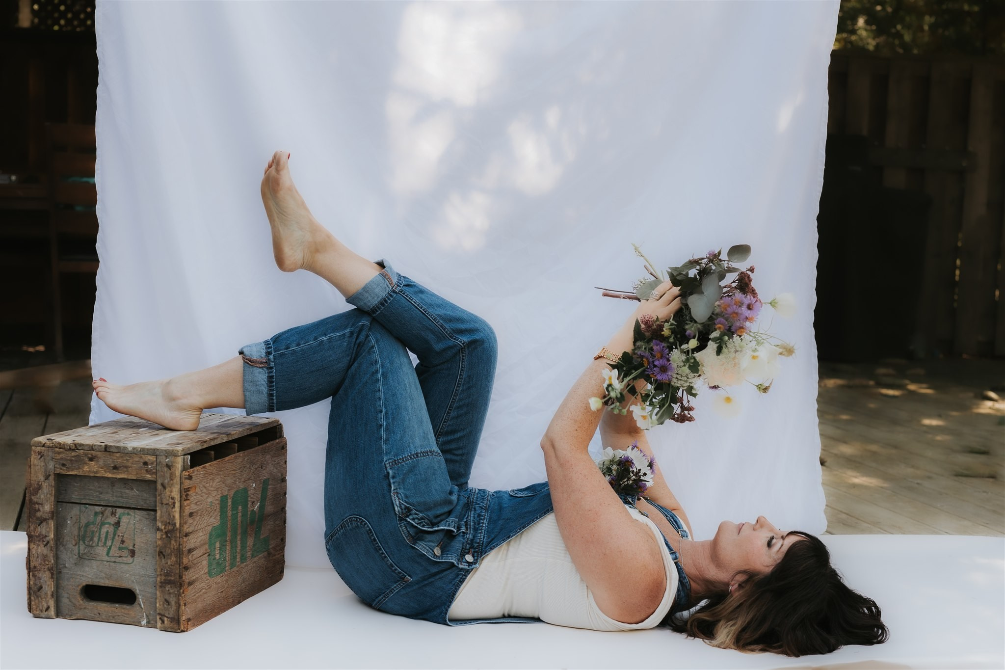 woman lays on floor on back holding flowers in the air and feet up in air