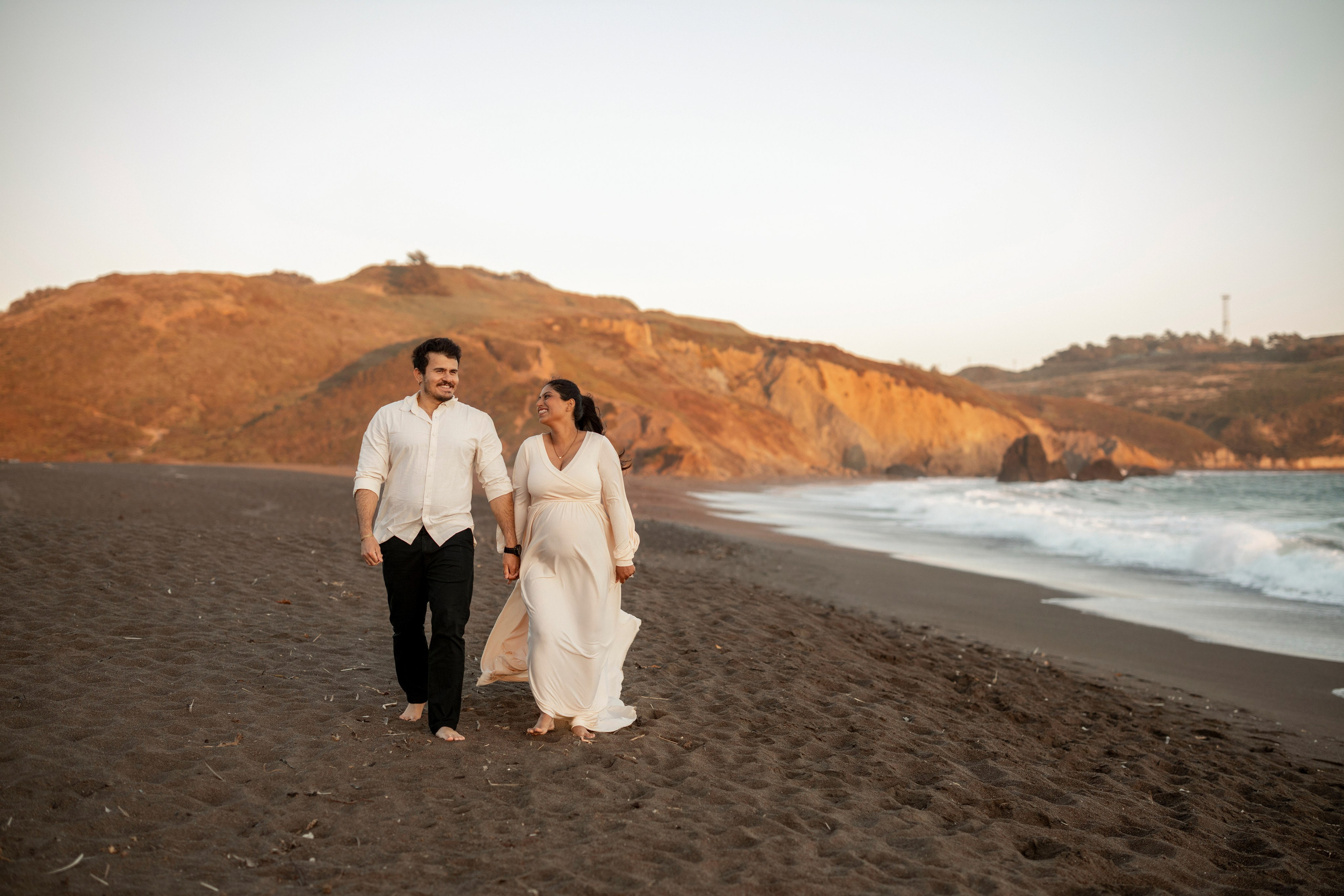Lifestyle beach maternity photography with expecting couple walking by water