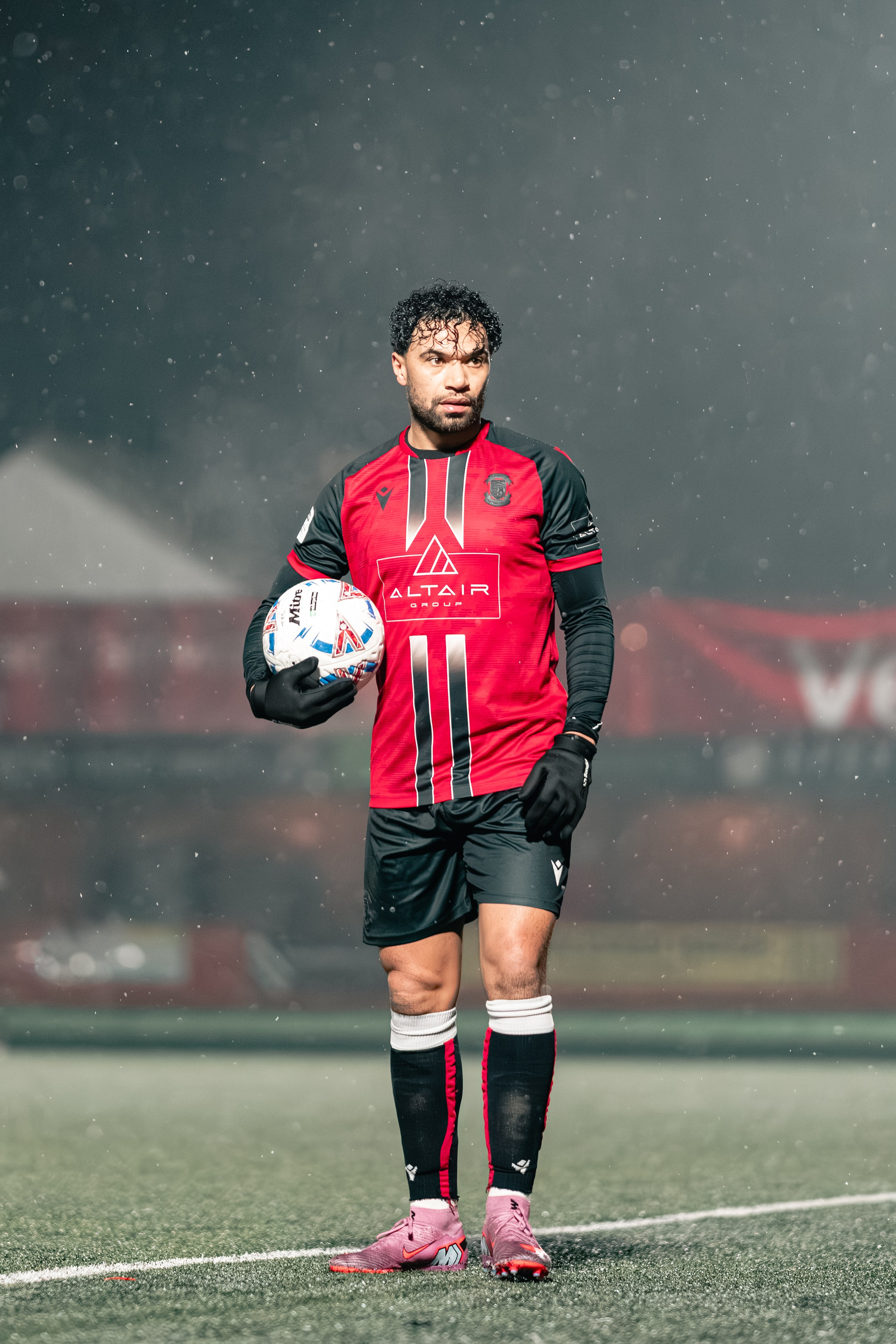 Luke Fairlamb of Tamworth FC holds the match ball under the floodlights in falling rain during the Birmingham Senior Cup tie vs Alvechurch at The Lamb Ground, Feb 3 2026.