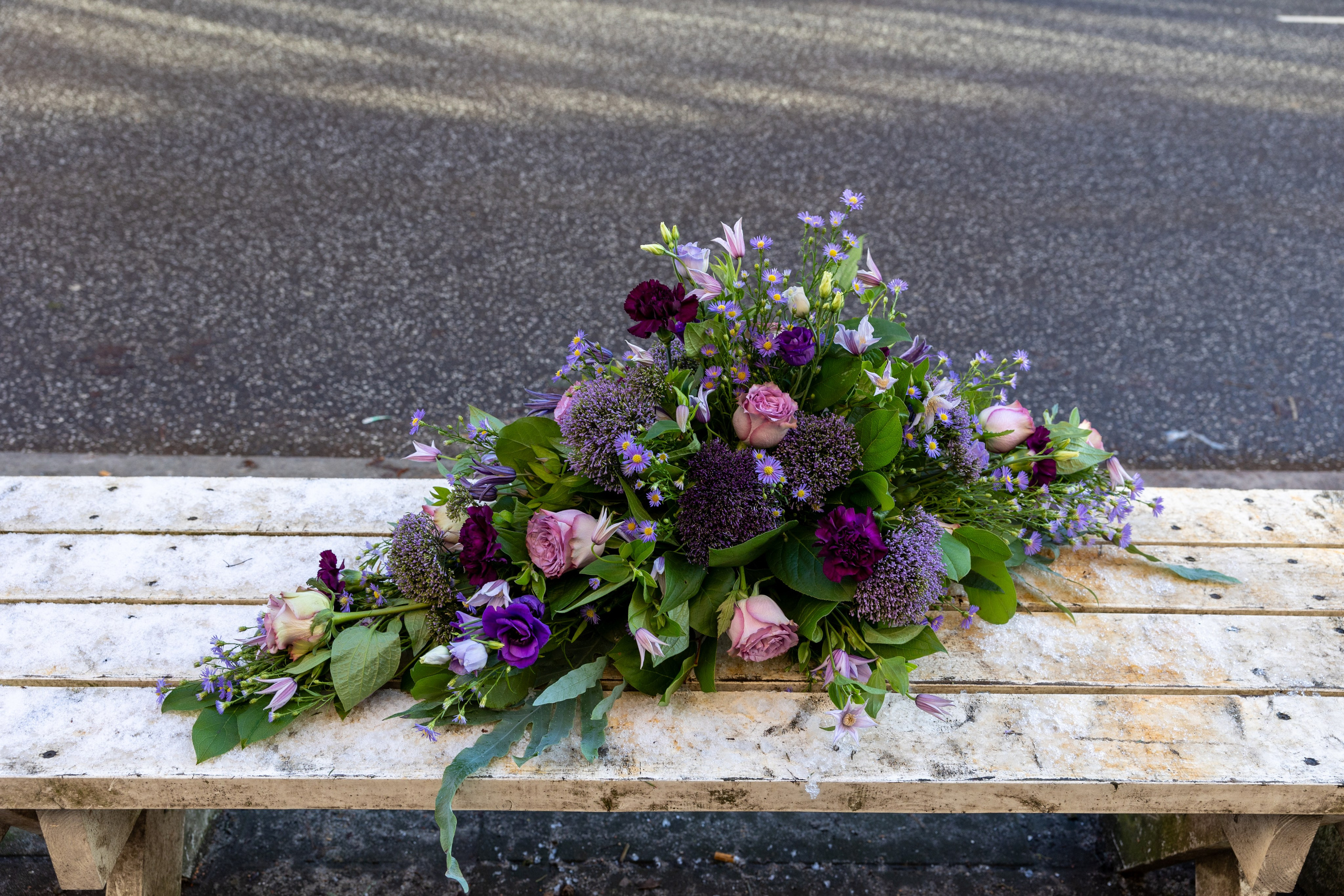 Smuk båredekoration til at ligge på kirkegulvet. Blomsterne er bundet tæt sammen, efter hinanden, i et flot blomsterflor i grønne-lilla nuancer. Denne unikke båredekoration er mere end bare en hilsen.