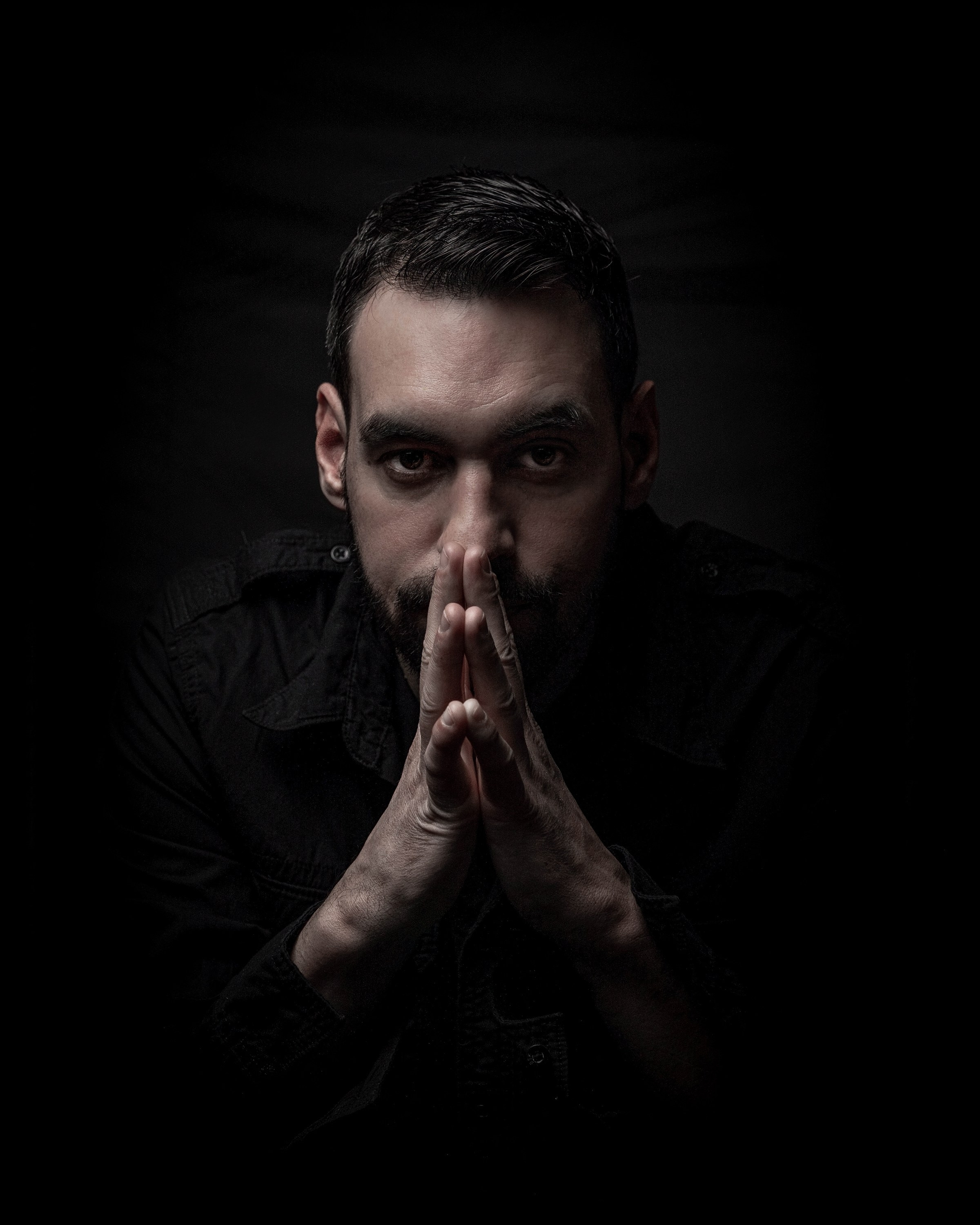 Dark moody portrait of a man with hands clasped near his face
