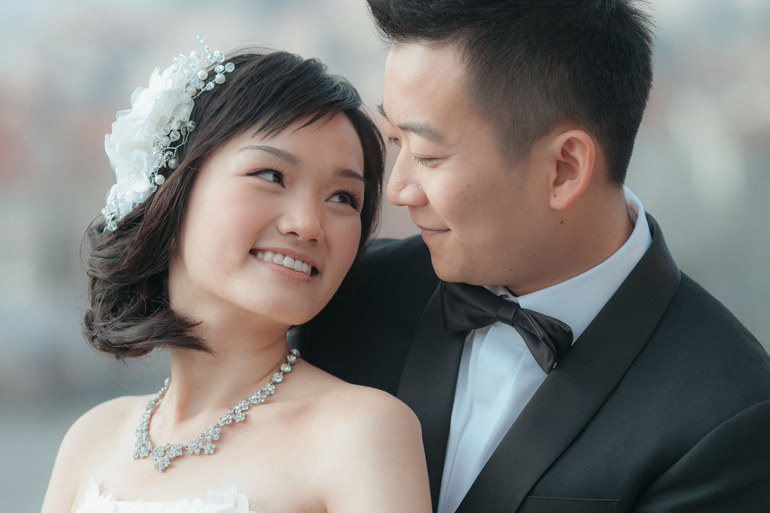 A close up portrait of a stylish Asian bride smiling towards her tuxedo-attired partner 
