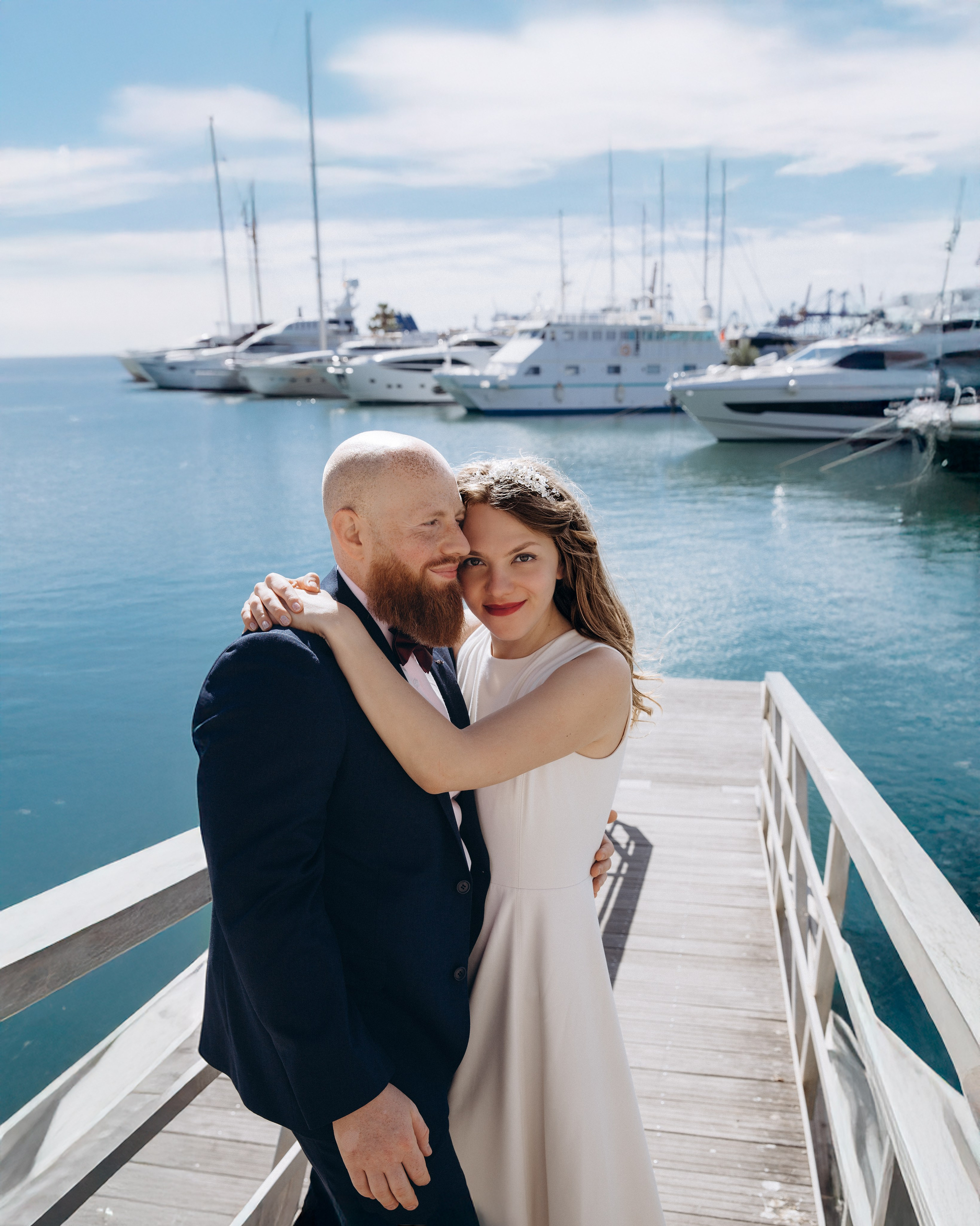 Romantic wedding photoshoot in Valencia, Spain — newlywed couple embracing on a wooden dock with a scenic marina backdrop and yachts in the background. Perfect for couples seeking elegant and waterfront wedding photography in Valencia and along the Spanish coast.