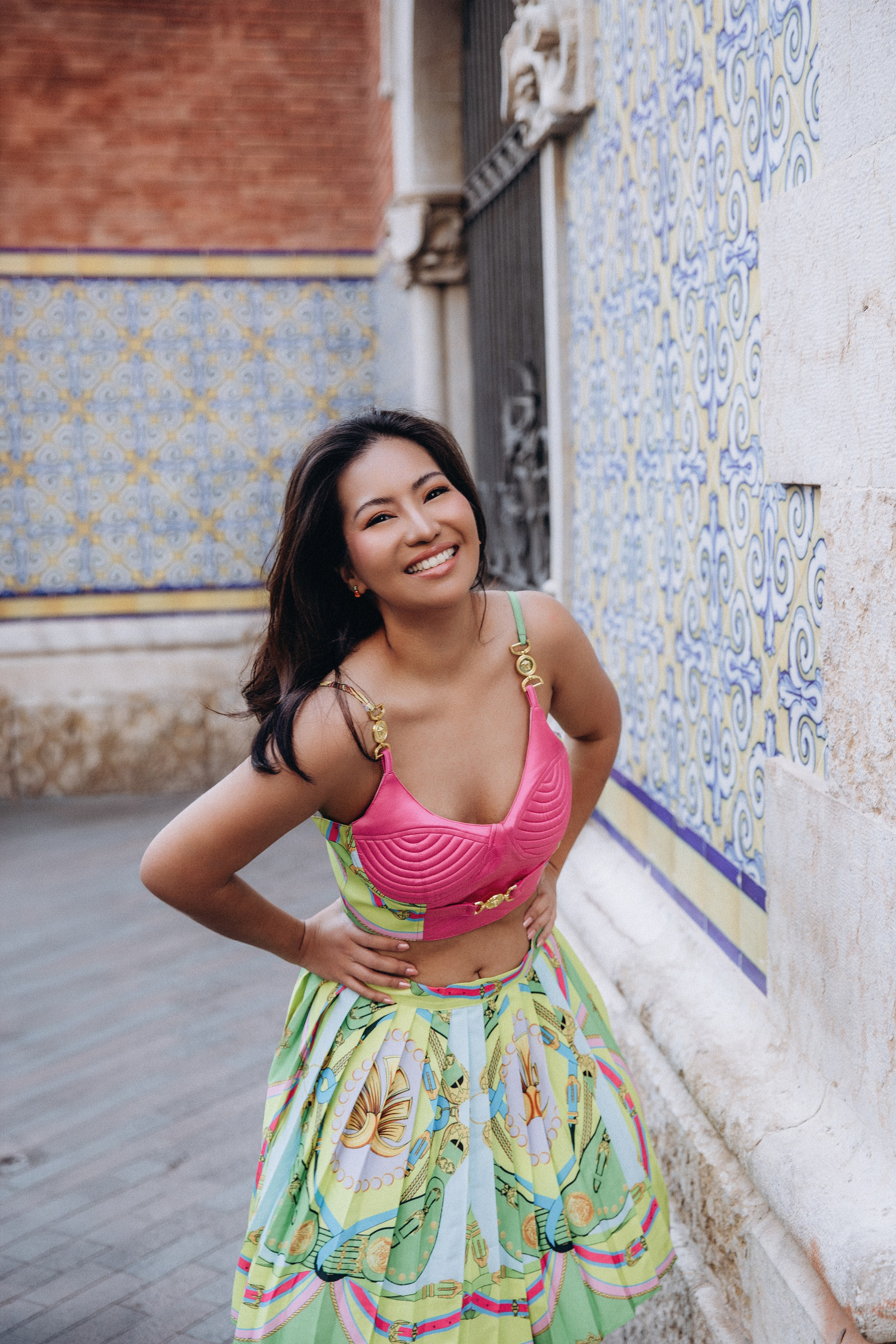 Sesión de retrato femenino en Valencia, España, con una mujer sonriente vestida con un colorido vestido de verano en una encantadora calle histórica con arquitectura mediterránea. Capturada con suave luz natural para crear un retrato vibrante, femenino y alegre. La imagen destaca la confianza, la personalidad y las emociones auténticas, ideal para fotografía de retrato femenino, sesiones lifestyle, marca personal y sesiones individuales en Valencia y toda España.
