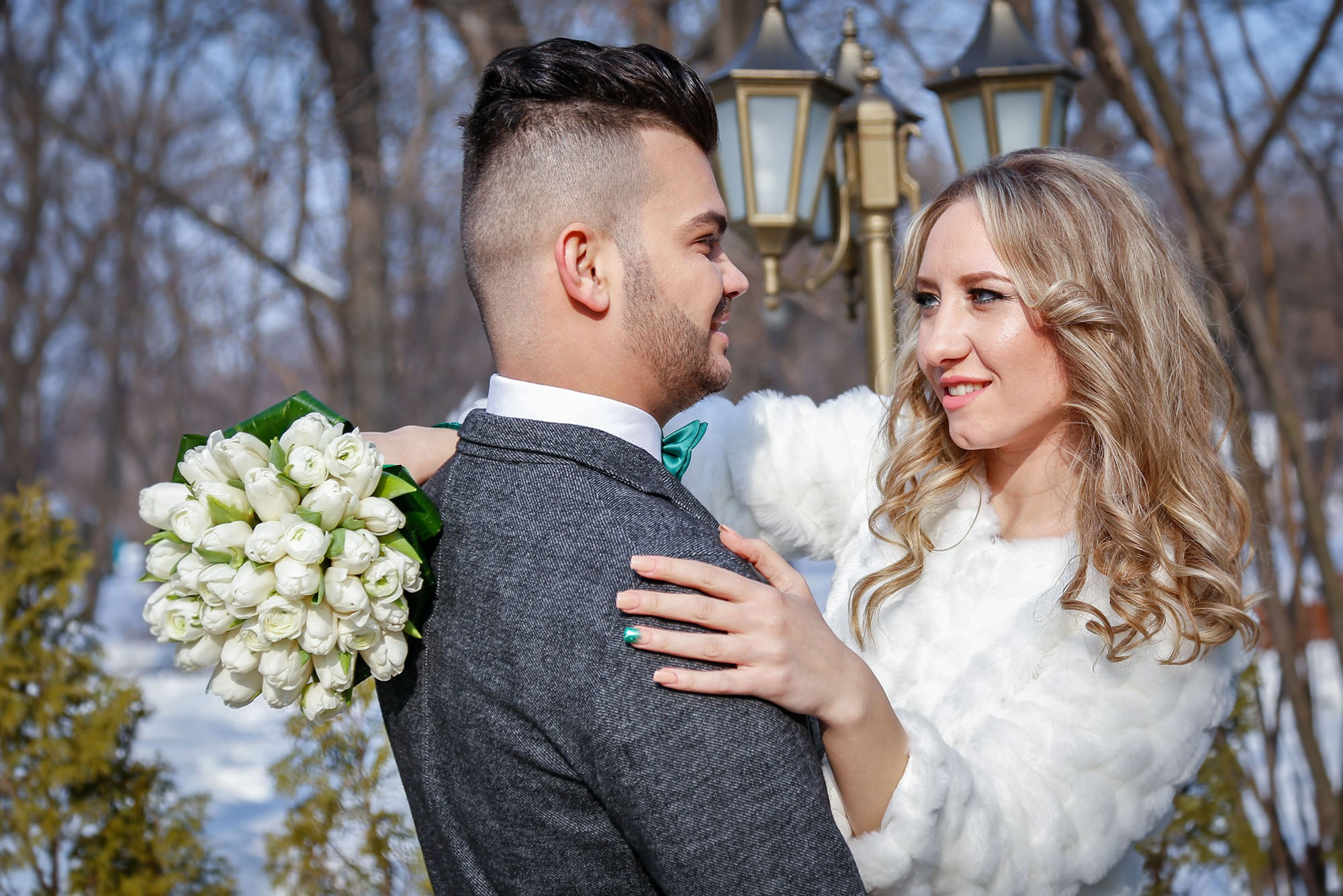 The groom embracing the bride from behind, a warm and romantic moment captured in the white scenery of the snowy park.
