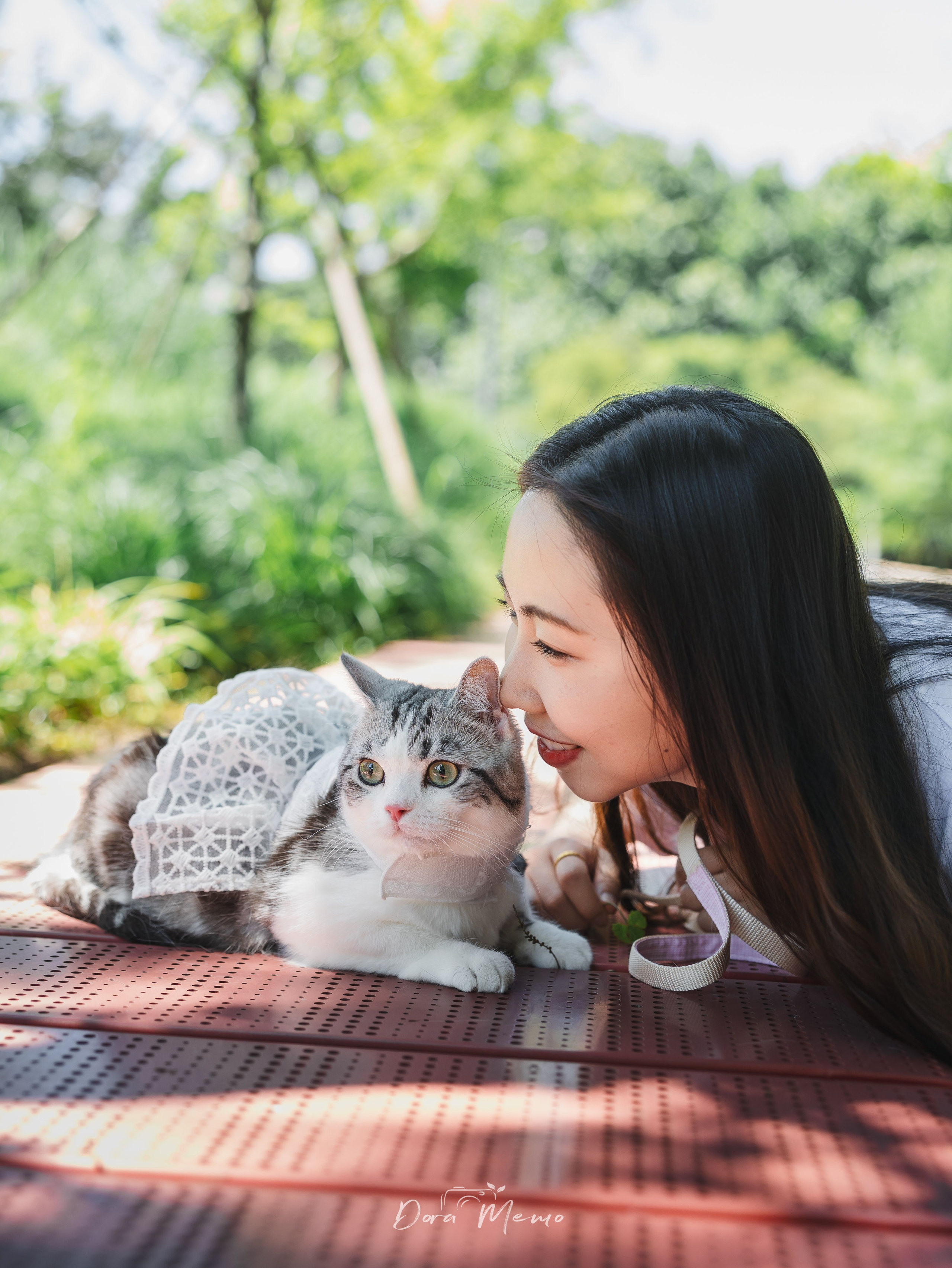 Woman nuzzling her cat's head, eyes closed, tender portrait in greenery