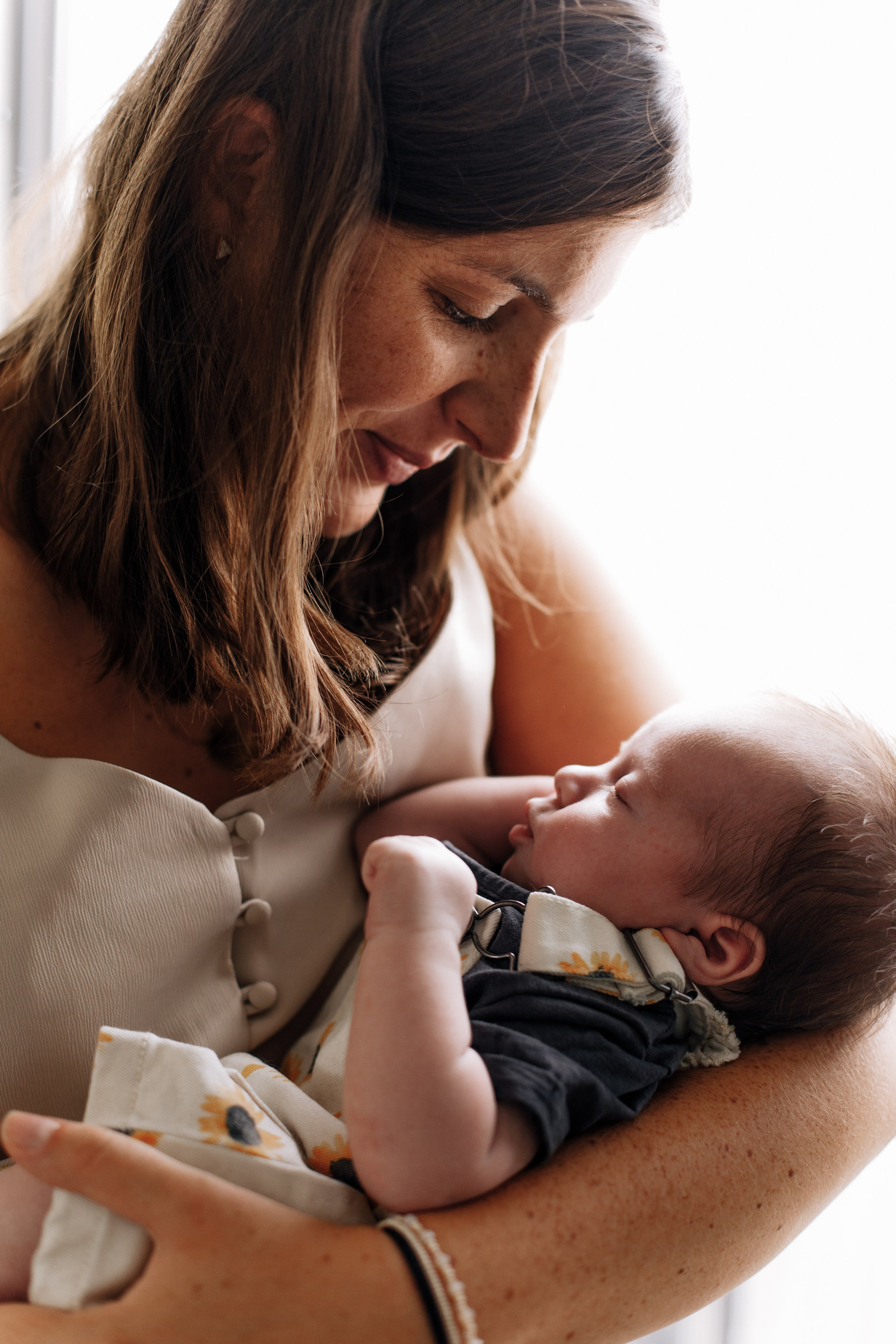 Mutter steht am Fenster und hält ihre Tochter im Arm.