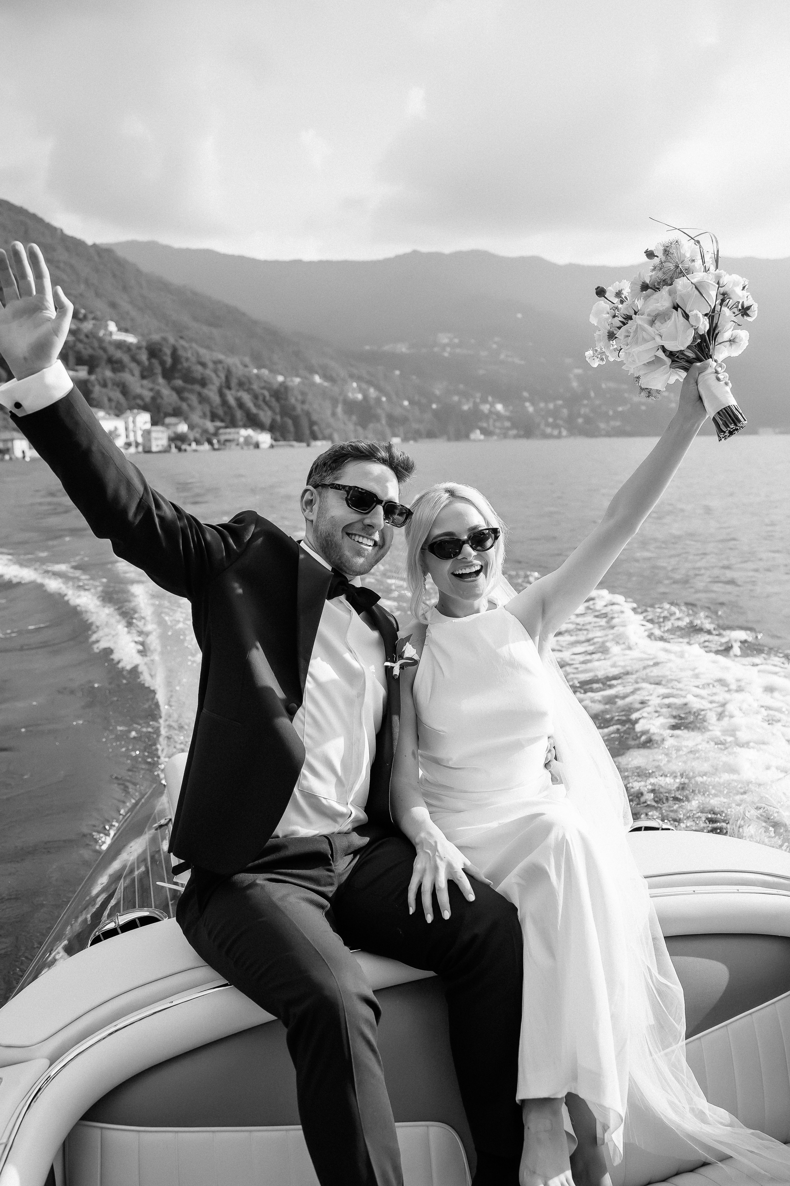 Black and white photo of the couple waving from the boat at Villa Lario, Lake Como, Italy