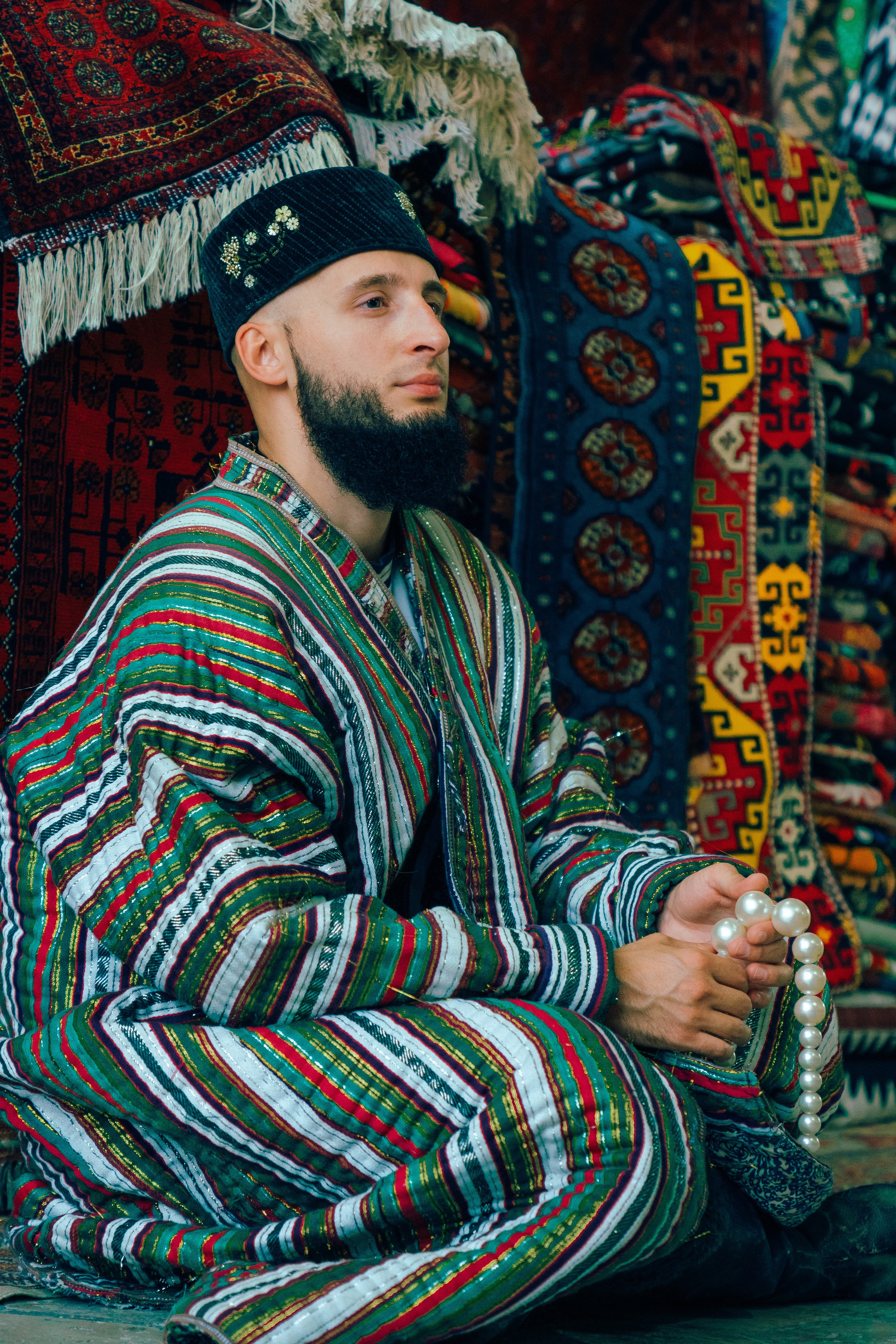 Национальный костюм Узбекистана для мужчин — традиционный чапан и тюбетейка в интерьере с коврами