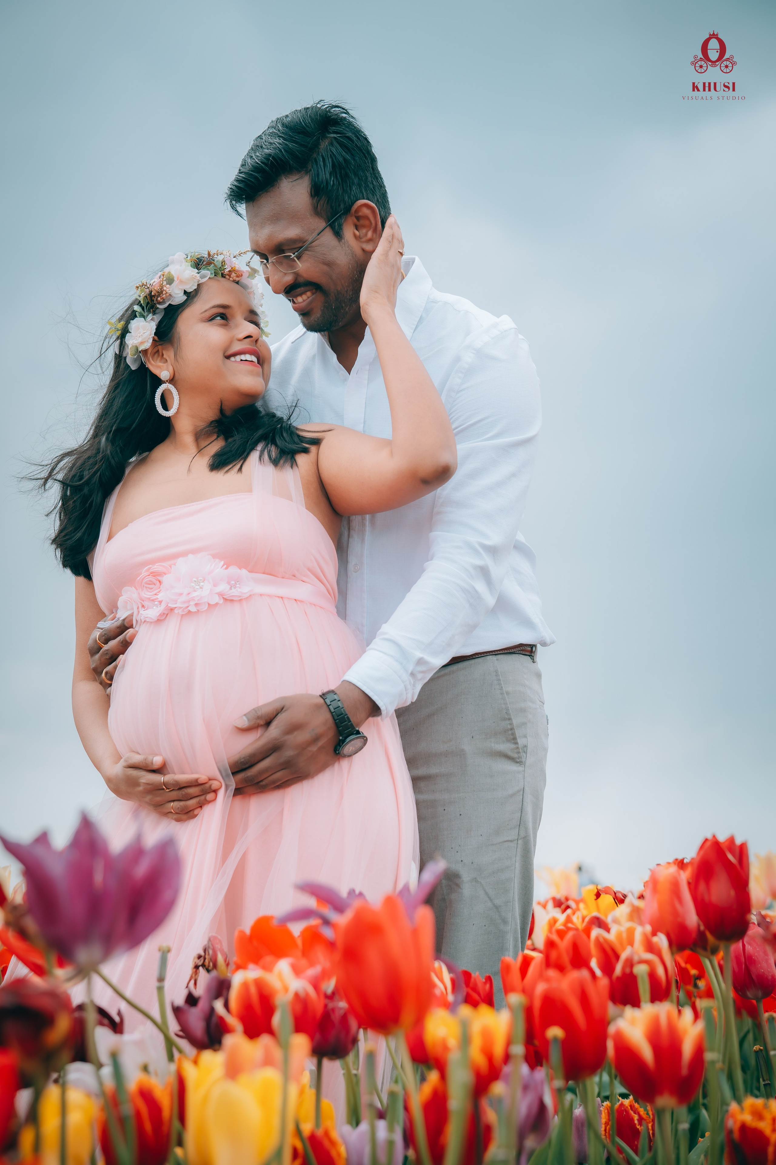 A pregnant woman holding her husband's face and looking at him and the man holding her from behind in a tulips in netherlands