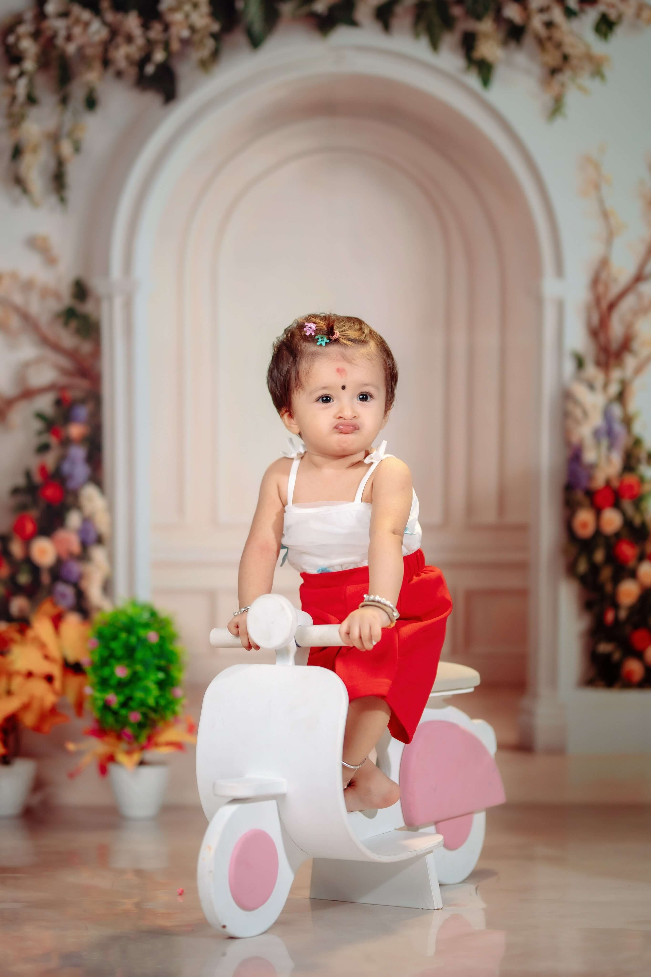 A baby girl posing on a white toy scooter for his milestone birthday photoshoot in Nepal
