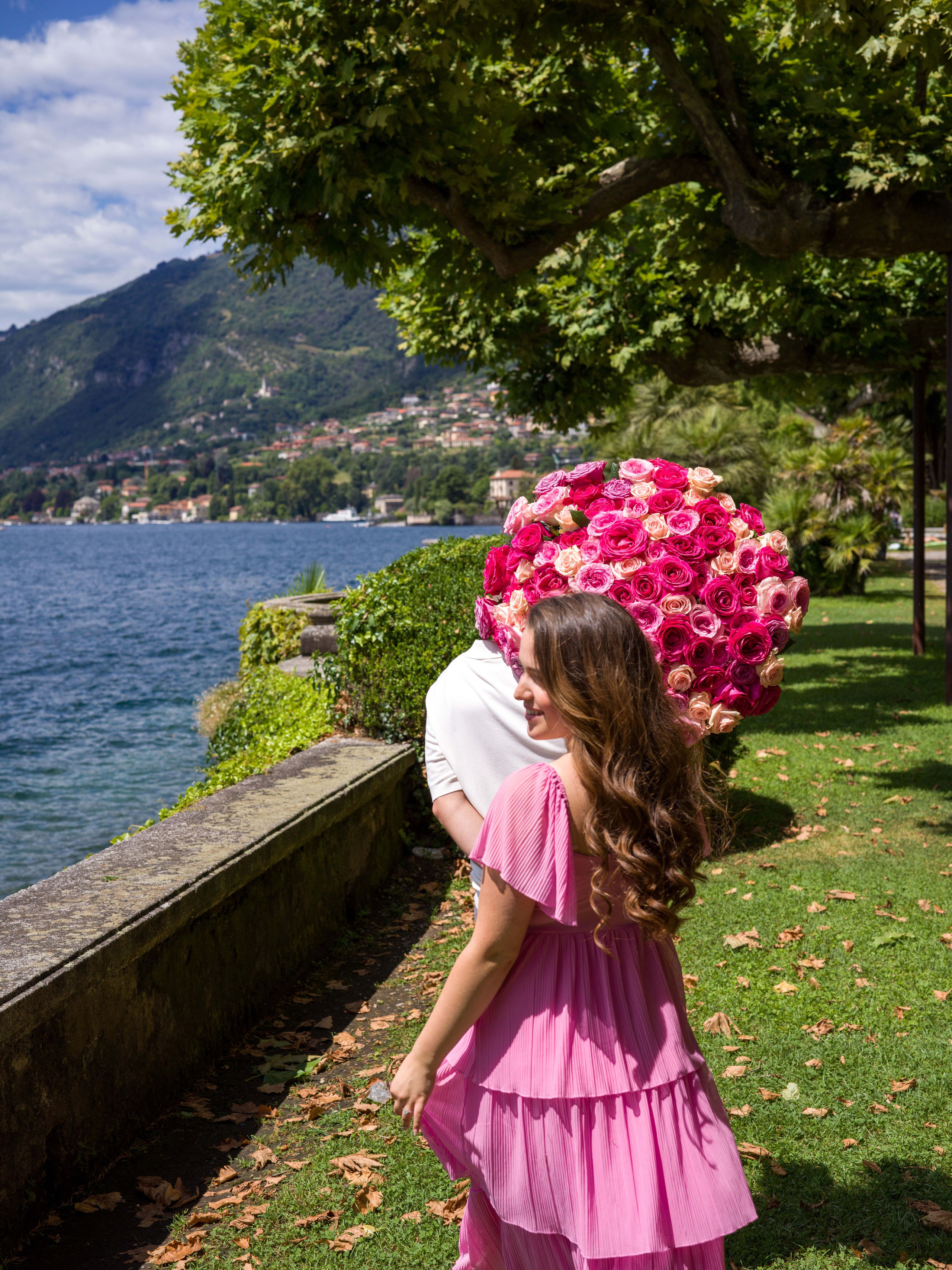 Proposal, Parco Civico Teresio Olivelli, Lake Como – bride-to-be covering her face with flowers, following him along the lakeshore
