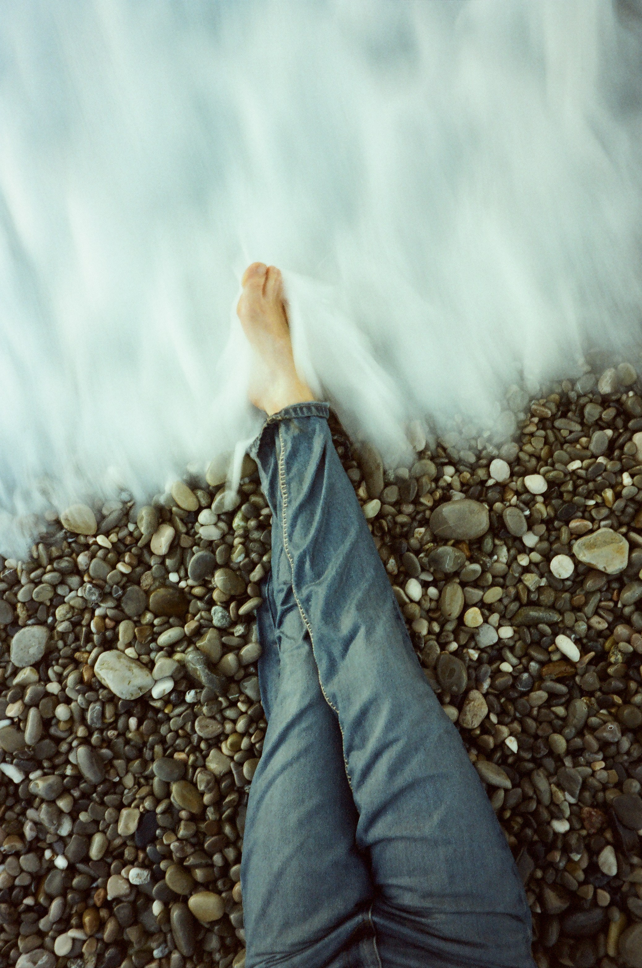 Fine art film photography, Nice, French Riviera – woman's legs in the sea as waves cover her feet at sunrise