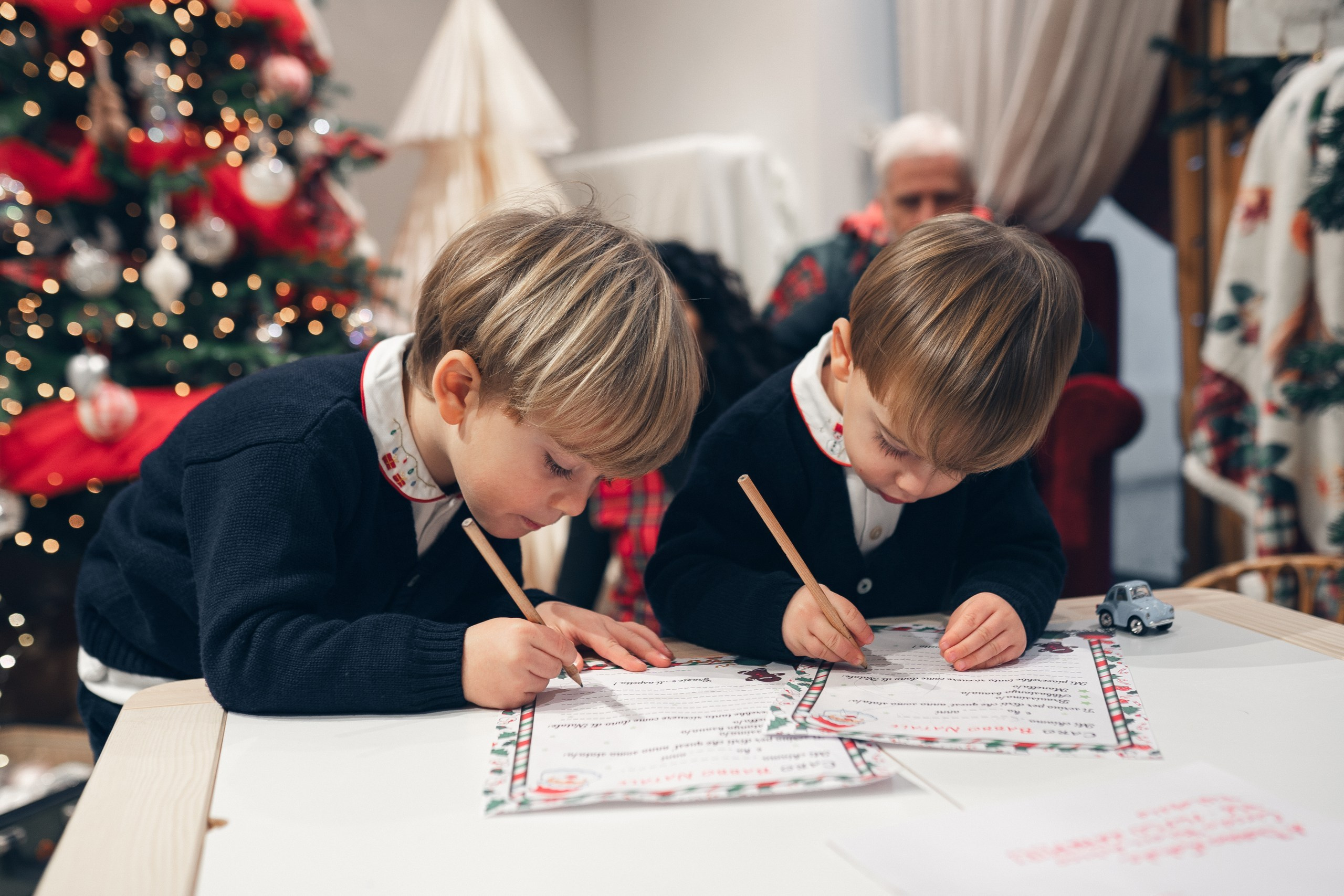 Bambino che scrive una letterina a Babbo Natale su un tavolo pieno di dolci natalizi