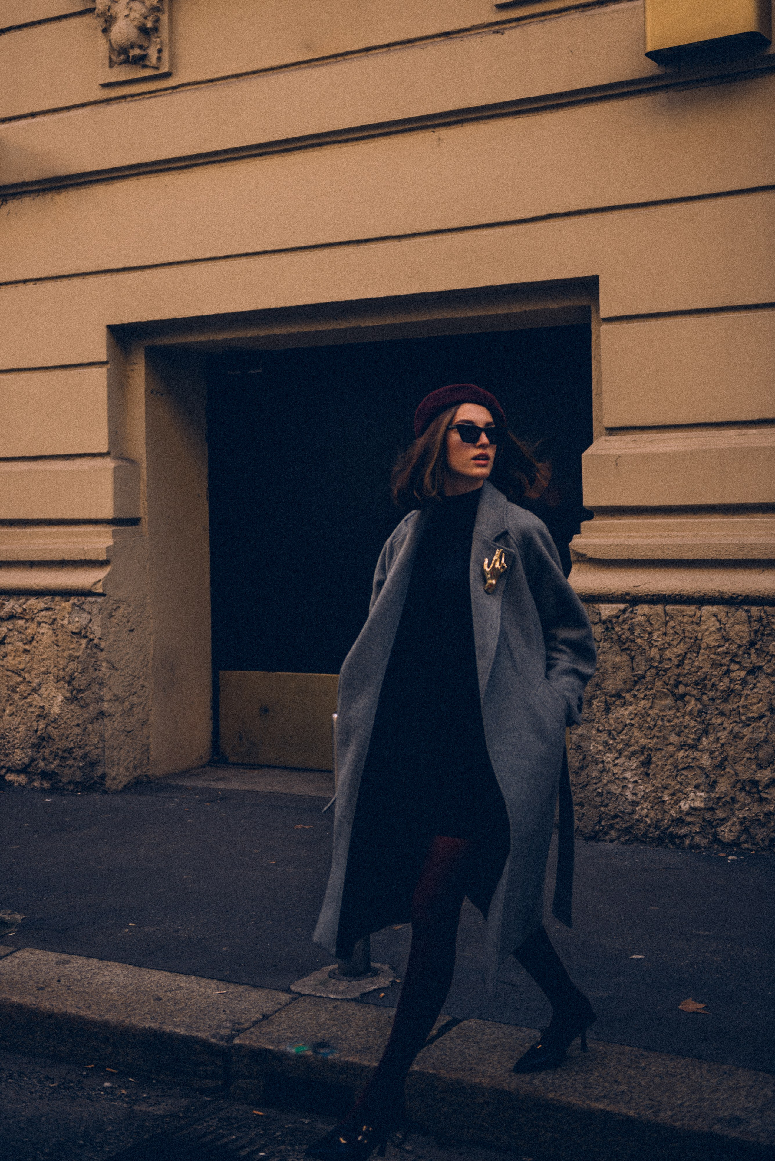 Urban elegance: woman in a stylish gray coat captured walking past a classic building in the heart of Milan