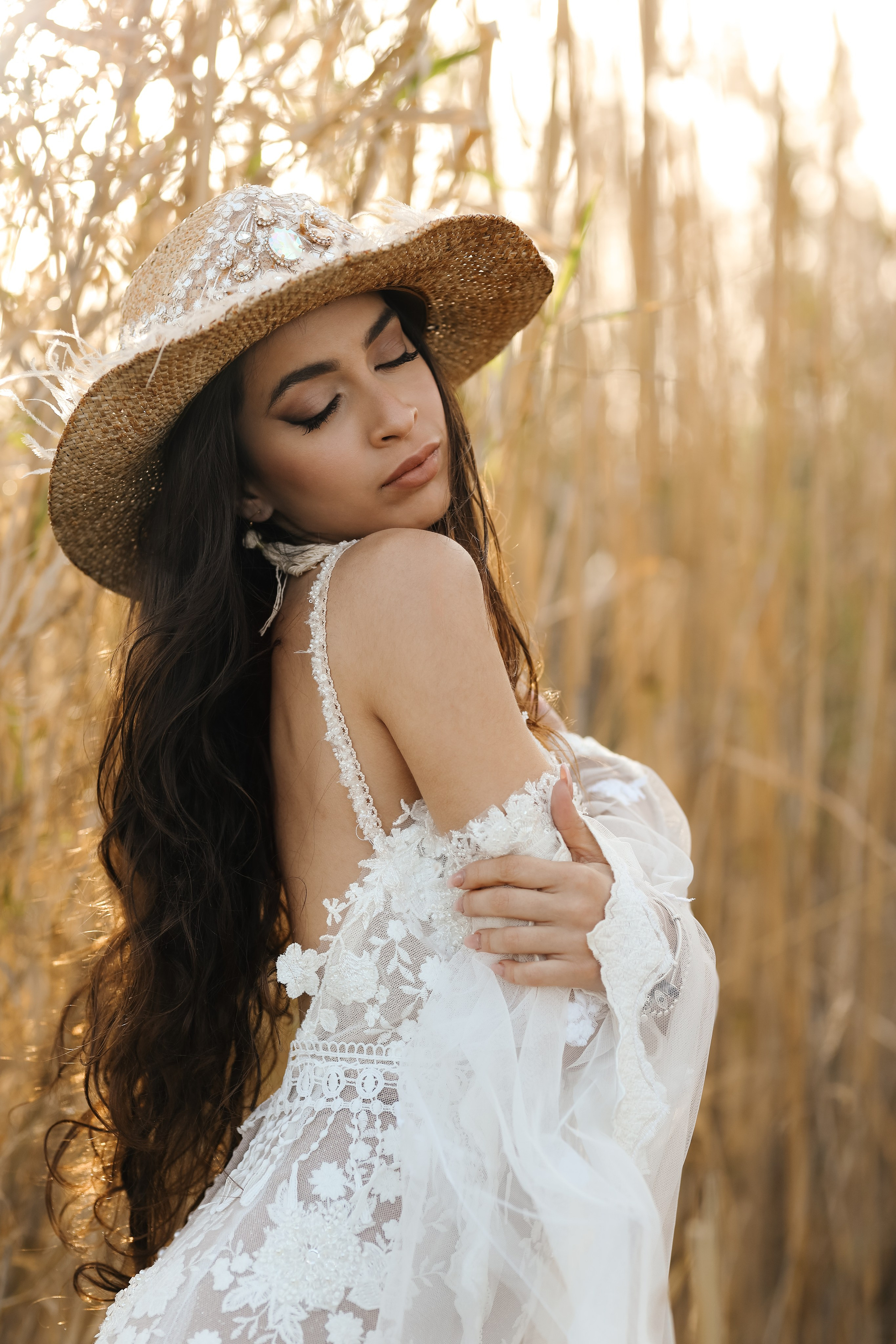 A portrait of girl in a wedding dress and a cowboy hat on a sunset background in reeds. Rhodes, Greece