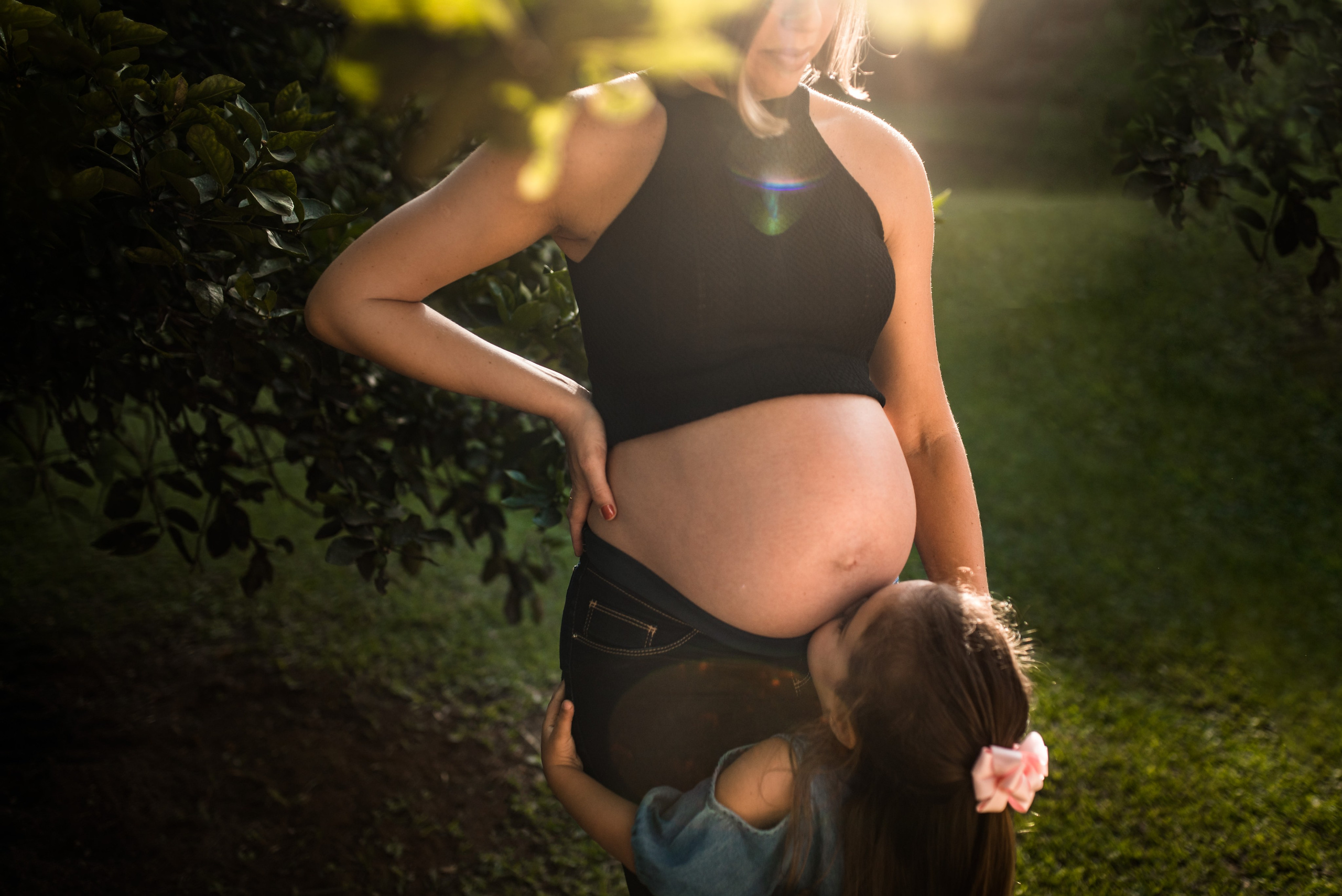Fotografia gestante lifestyle em Juiz de Fora, filha beijando a barriga da mãe ao entardecer