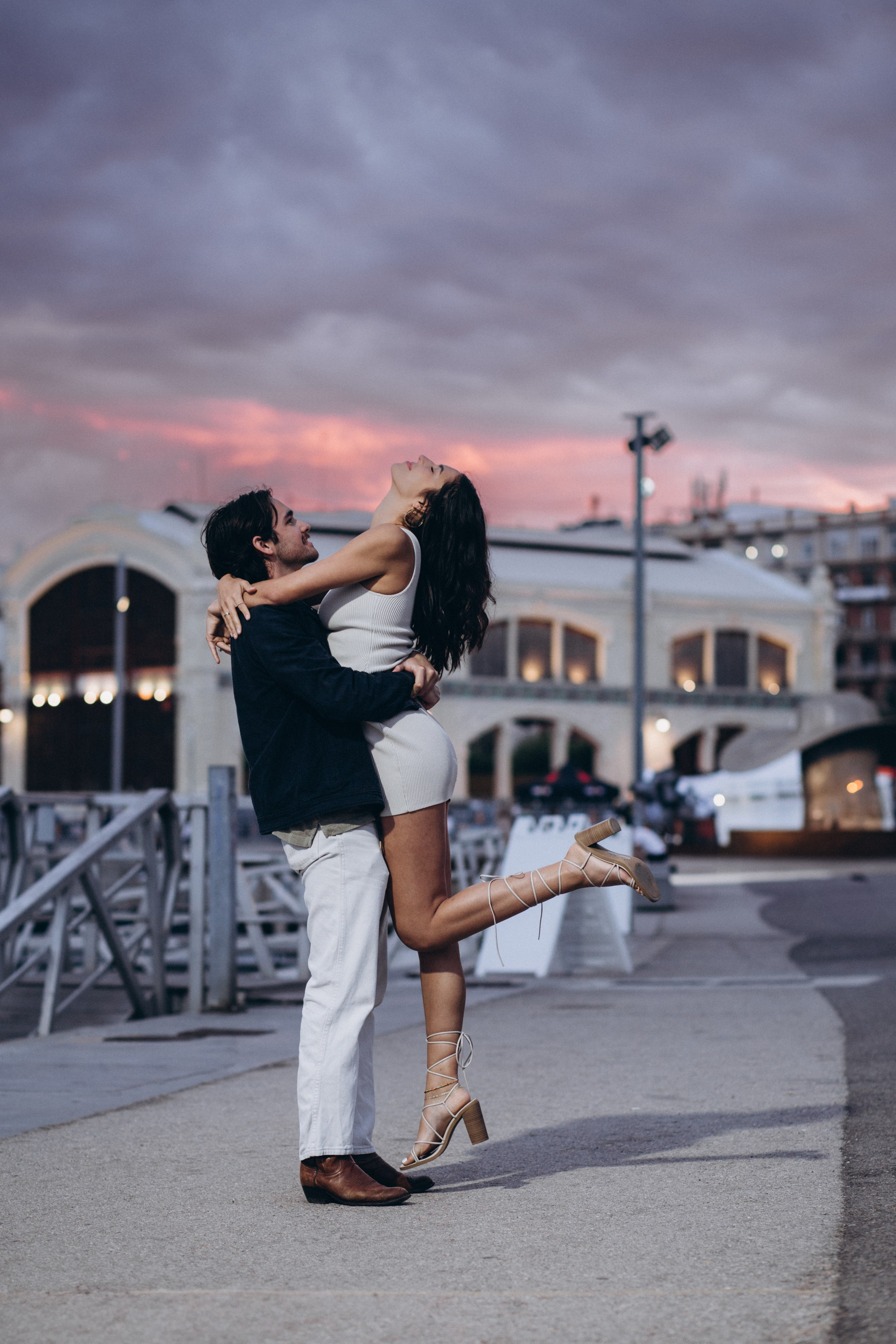 Romantic sunset couple photoshoot in Valencia, Spain — joyful moment of a man lifting his partner in a warm embrace against a dramatic evening sky. Ideal for couples searching for emotional, love-filled photography sessions or planning a love story photoshoot in Valencia and across Spain.