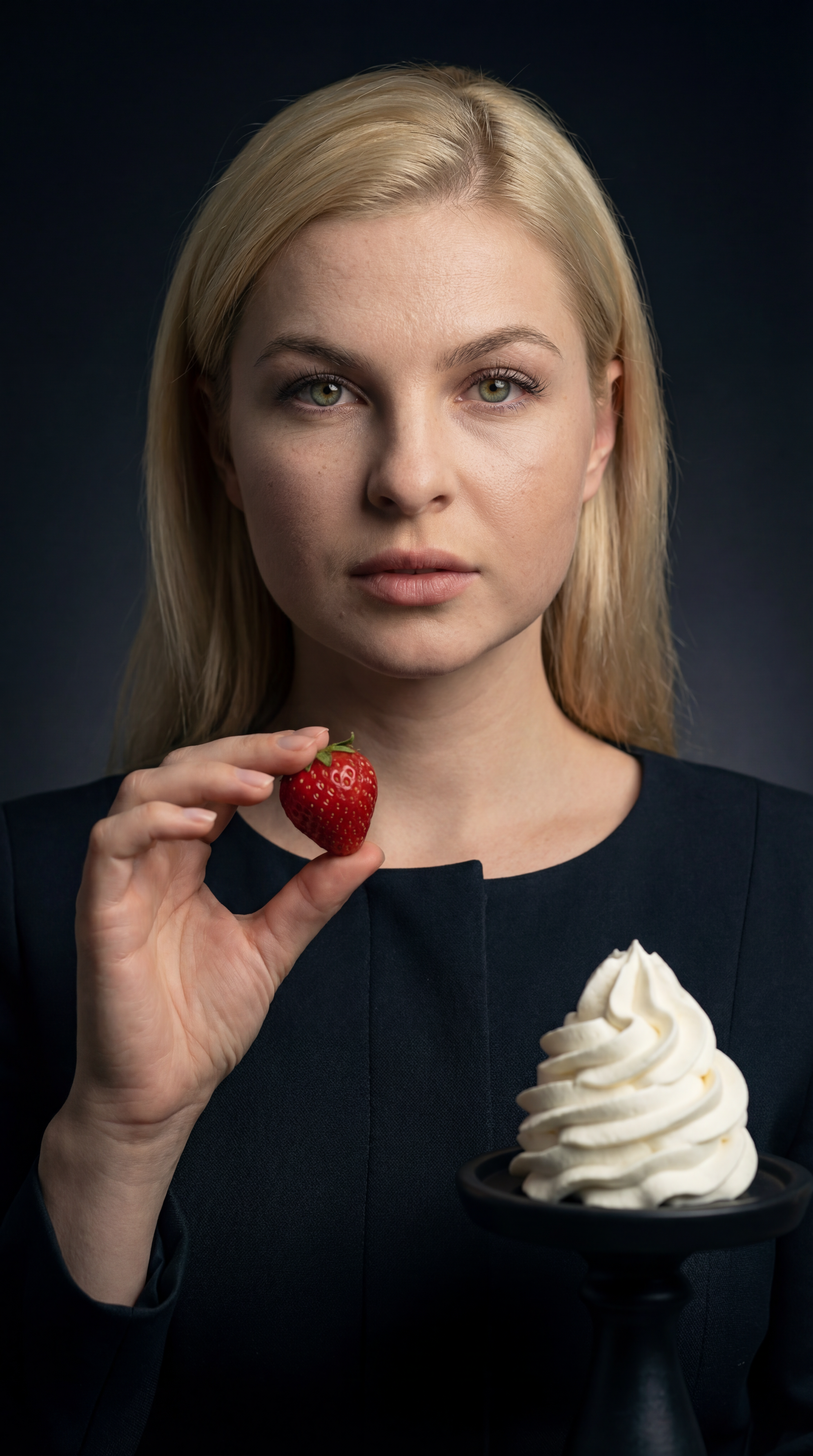 Blonde woman holding fresh strawberry next to whipped cream swirl on dark background, minimalist studio portrait photography, dramatic lighting, food concept portrait with strawberry and cream