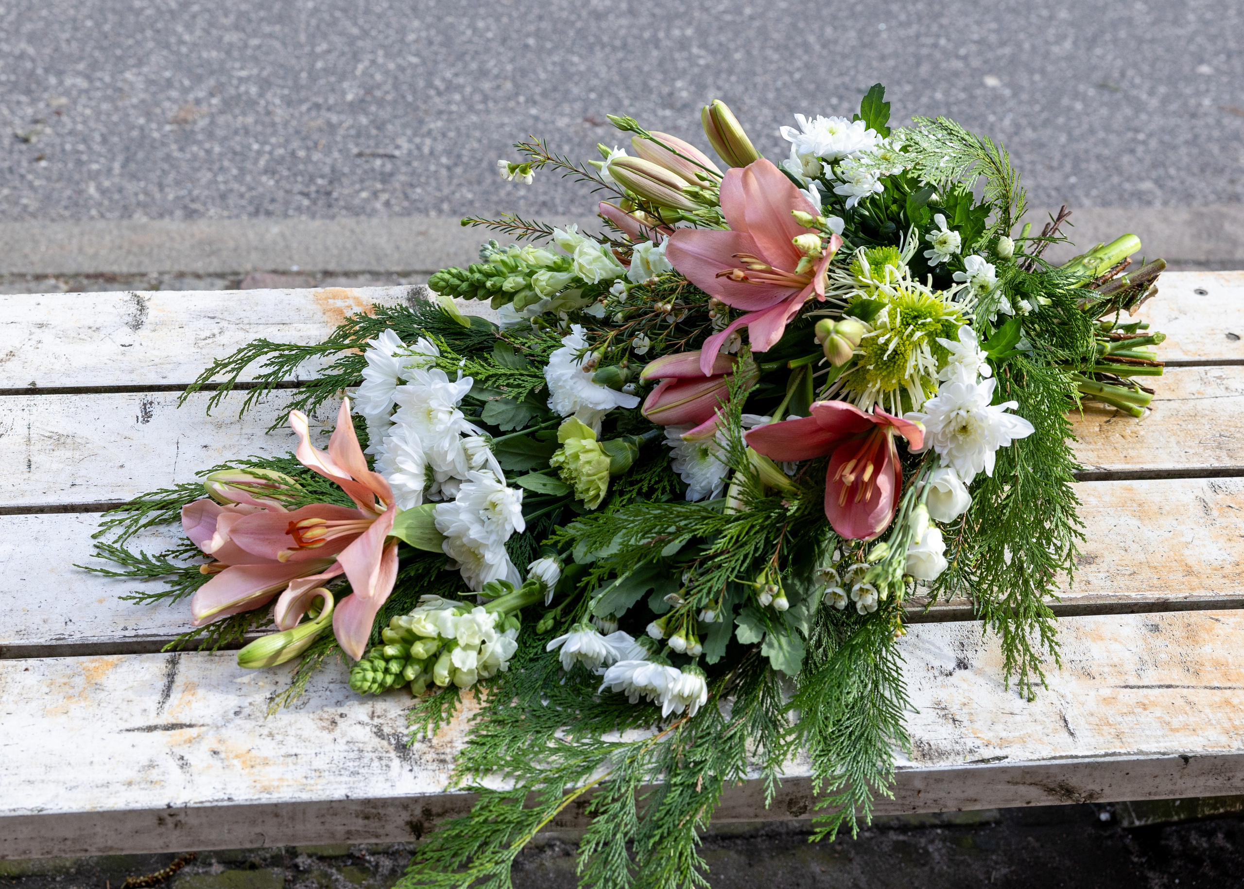 En tidløs bårebuket, hvor blomsterne er tæt bundet i nuancer af lyserød og hvid. Denne klassiske buket passer til alle årstider og udgør en smuk sidste hilsen.